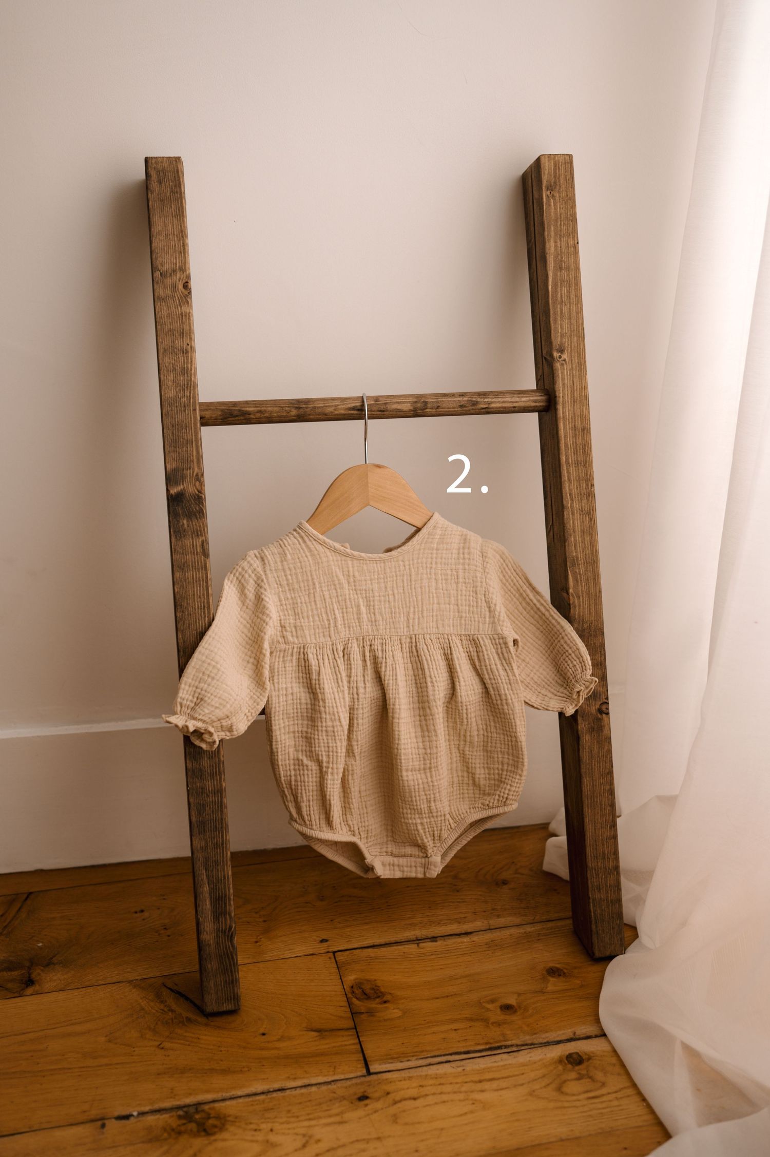 Beige linen crop top displayed on rustic wooden ladder against white wall in minimalist styling setup.