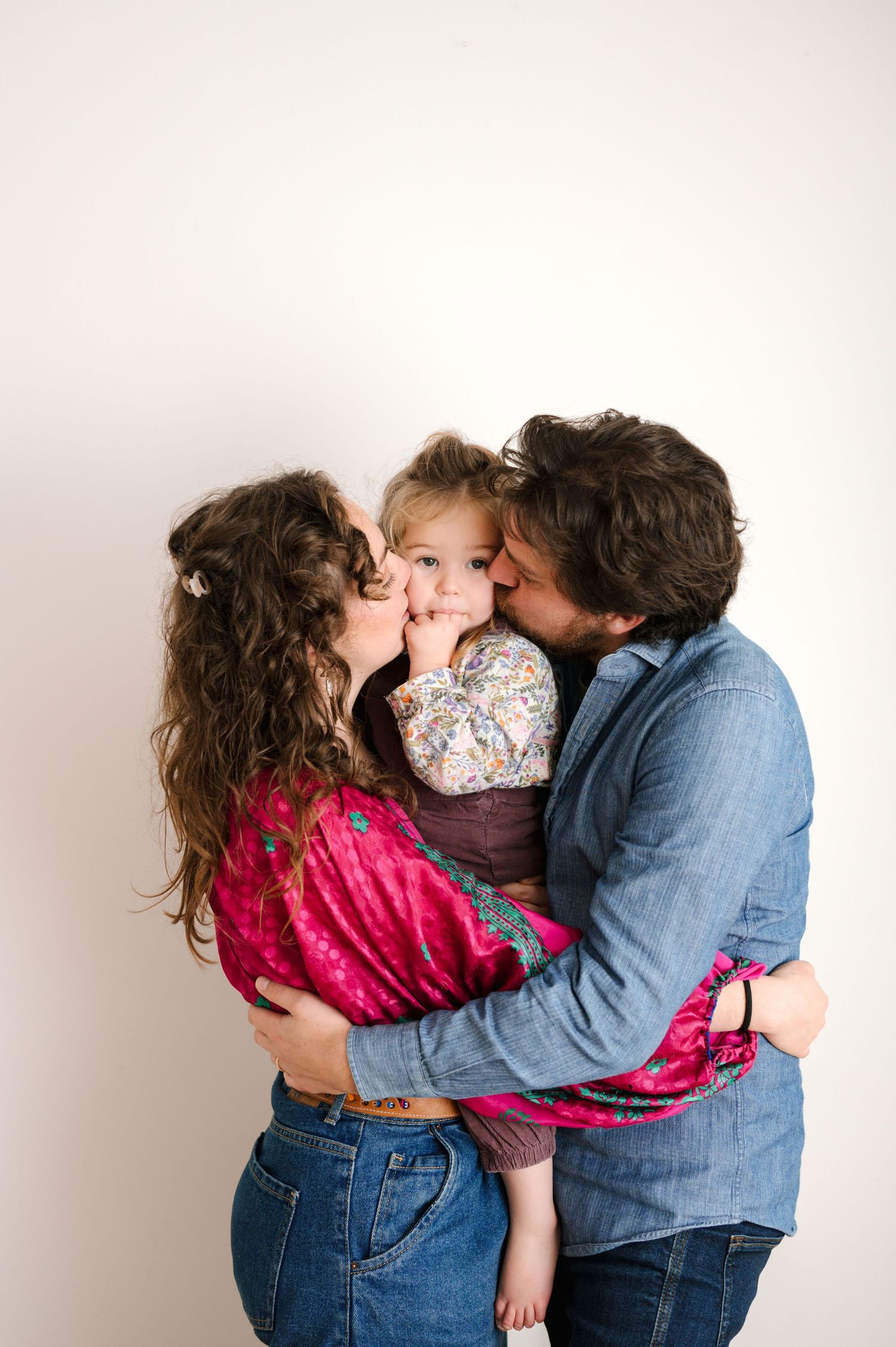 A sweet family moment captured in a series of photos showing parents kissing their child from both sides.