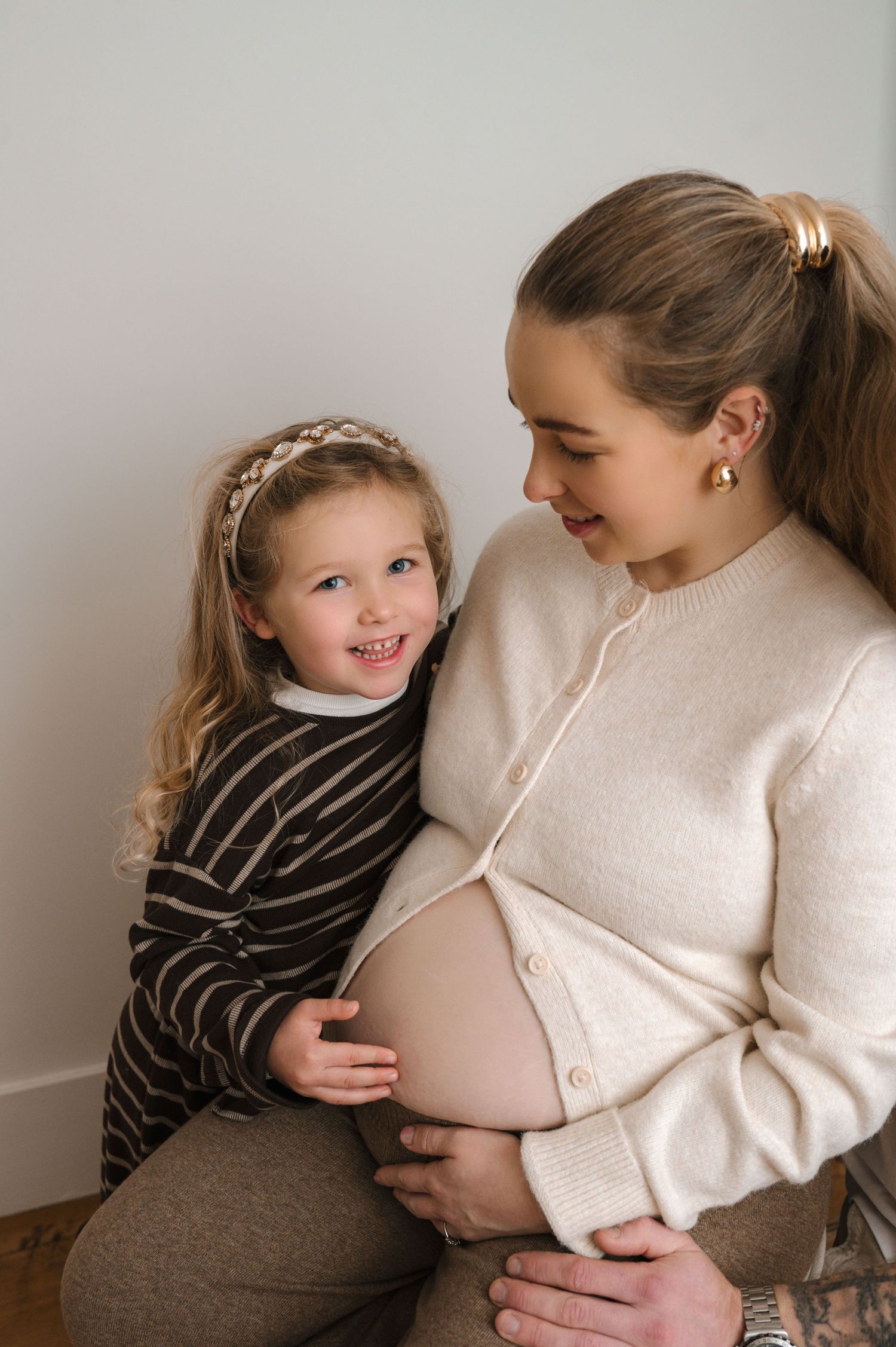 A heartwarming series of photos showing a young child gently touching and bonding with a pregnant belly in a cream sweater.