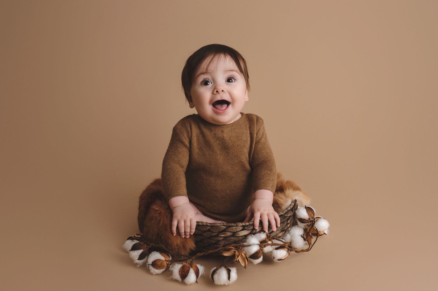 A small child sits on a brown backdrop surrounded by fluffy cotton decorations.