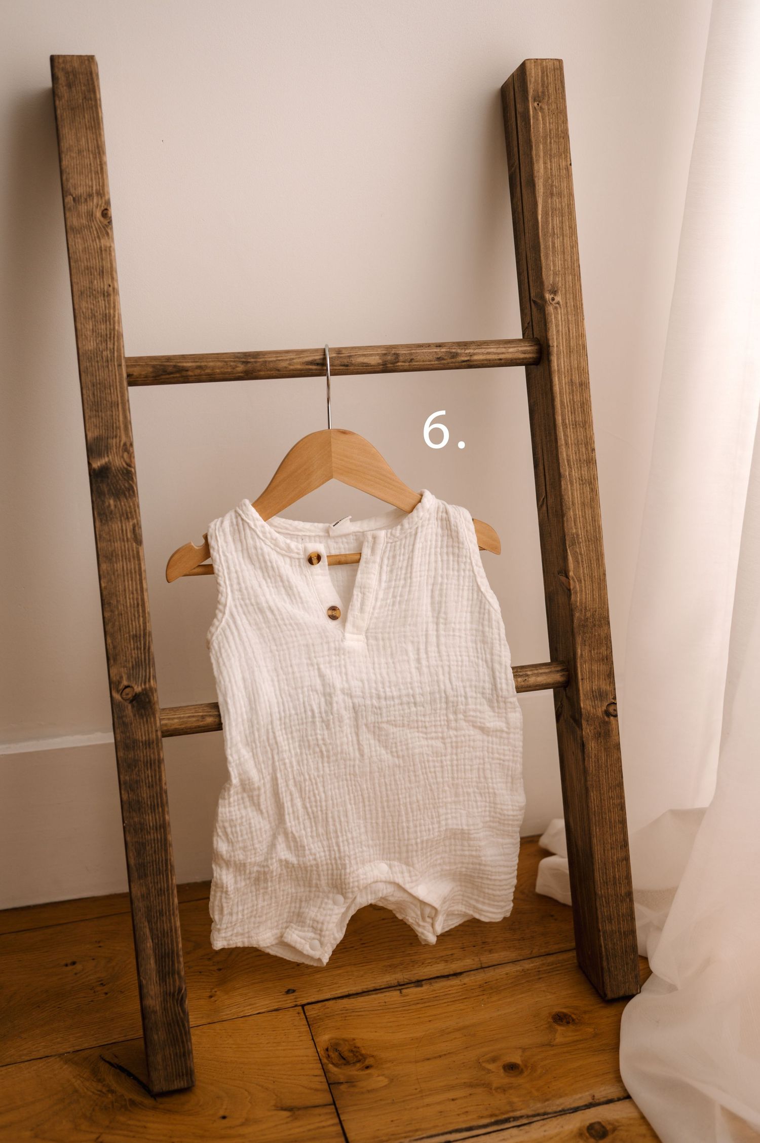White cotton garments hanging on rustic wooden beams against a light colored wall with hardwood flooring below.