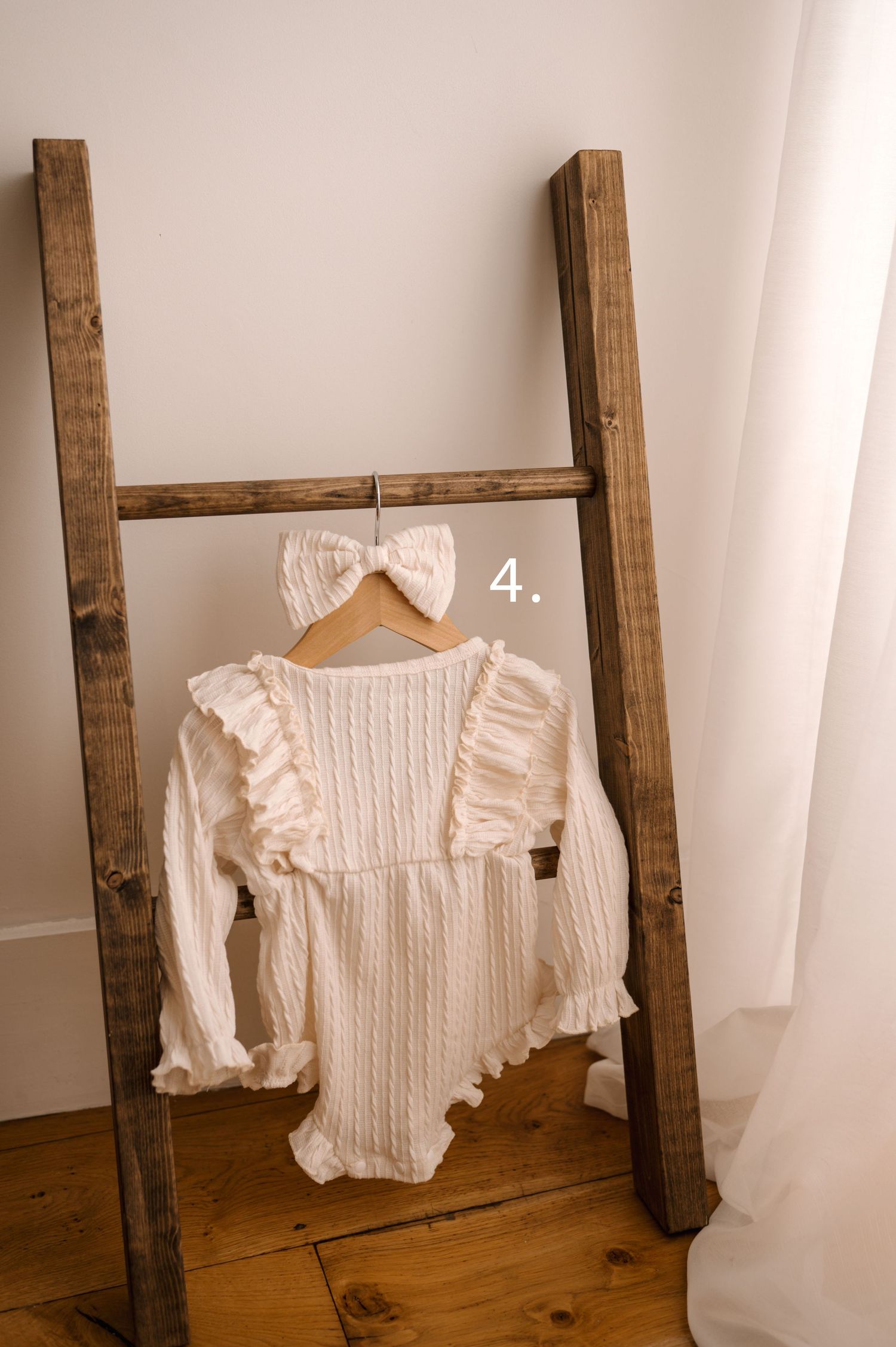 White knitted sweater with ruffled details displayed on wooden hangers against a white wall.