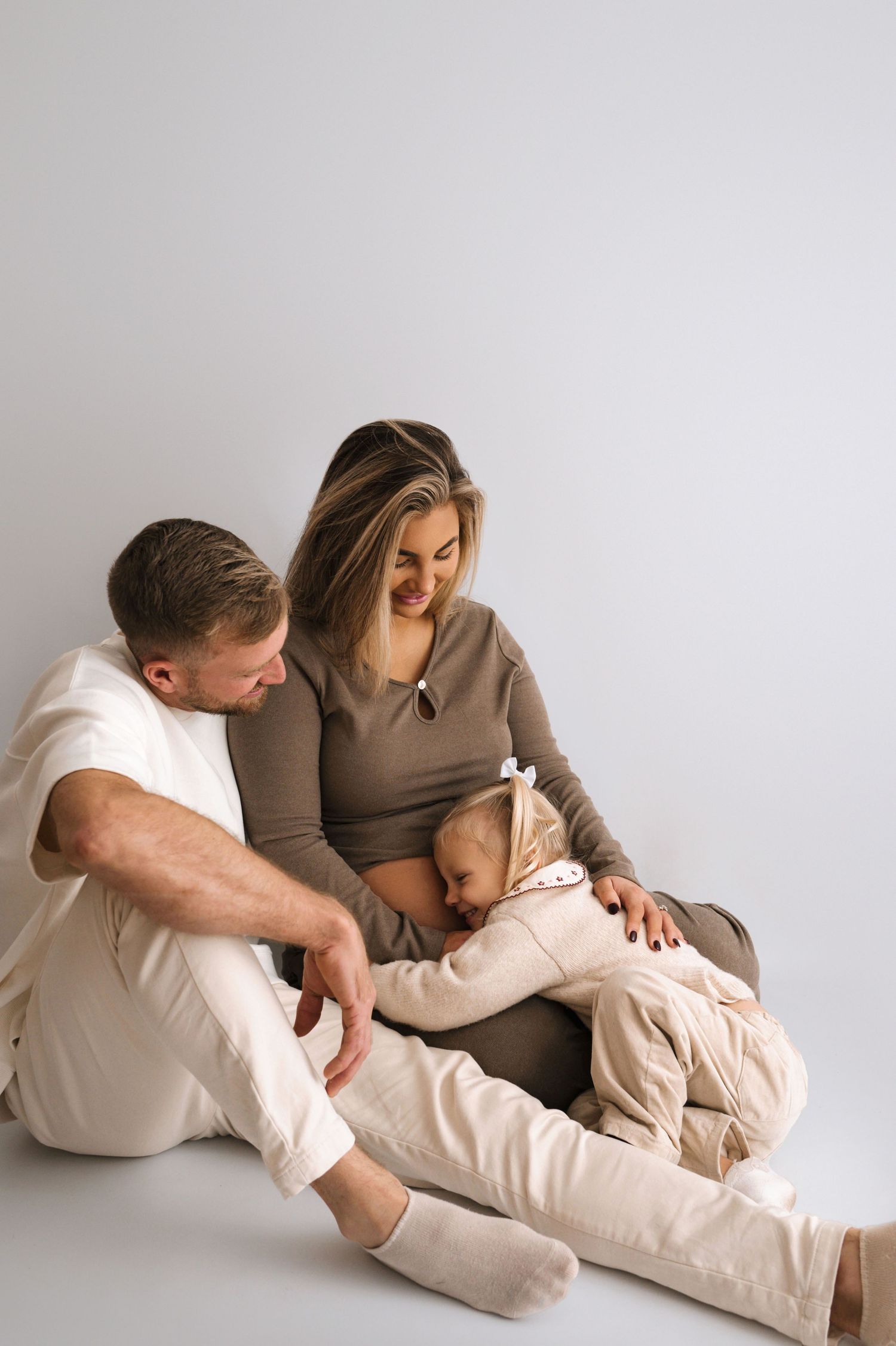 A series of intimate maternity photos showing a couple in neutral tones embracing on a white background.