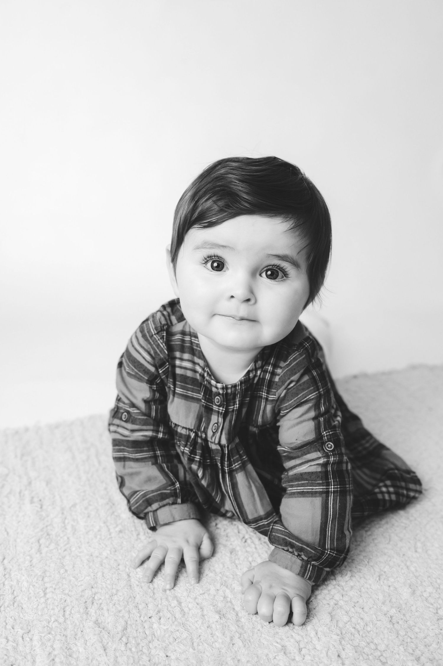 Black and white photo series of a baby in plaid shirt lying on carpet with sweet round-eyed expressions.