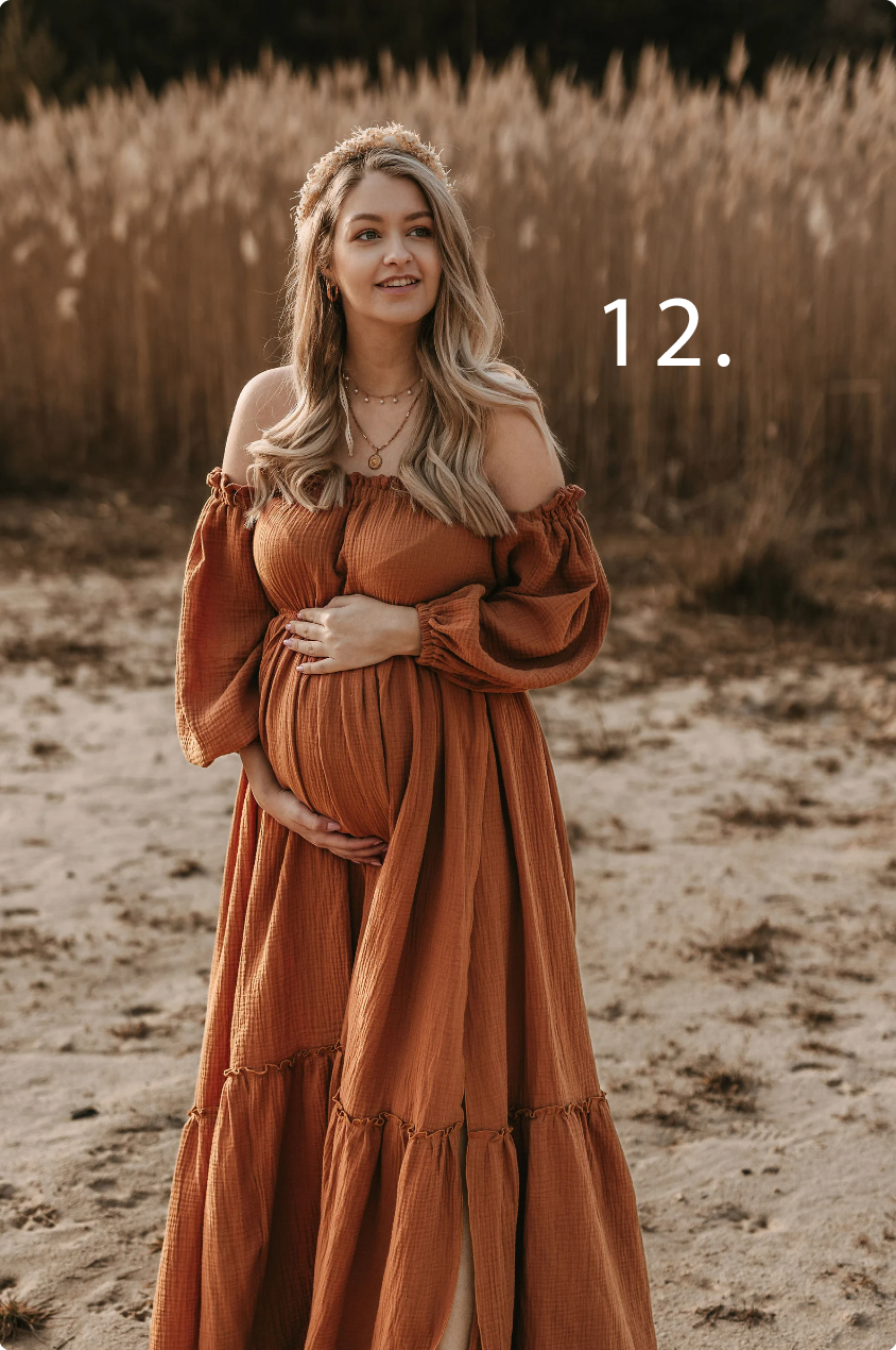 Maternity photo session in a rustic field with model wearing flowing rust-colored dress at sunset.