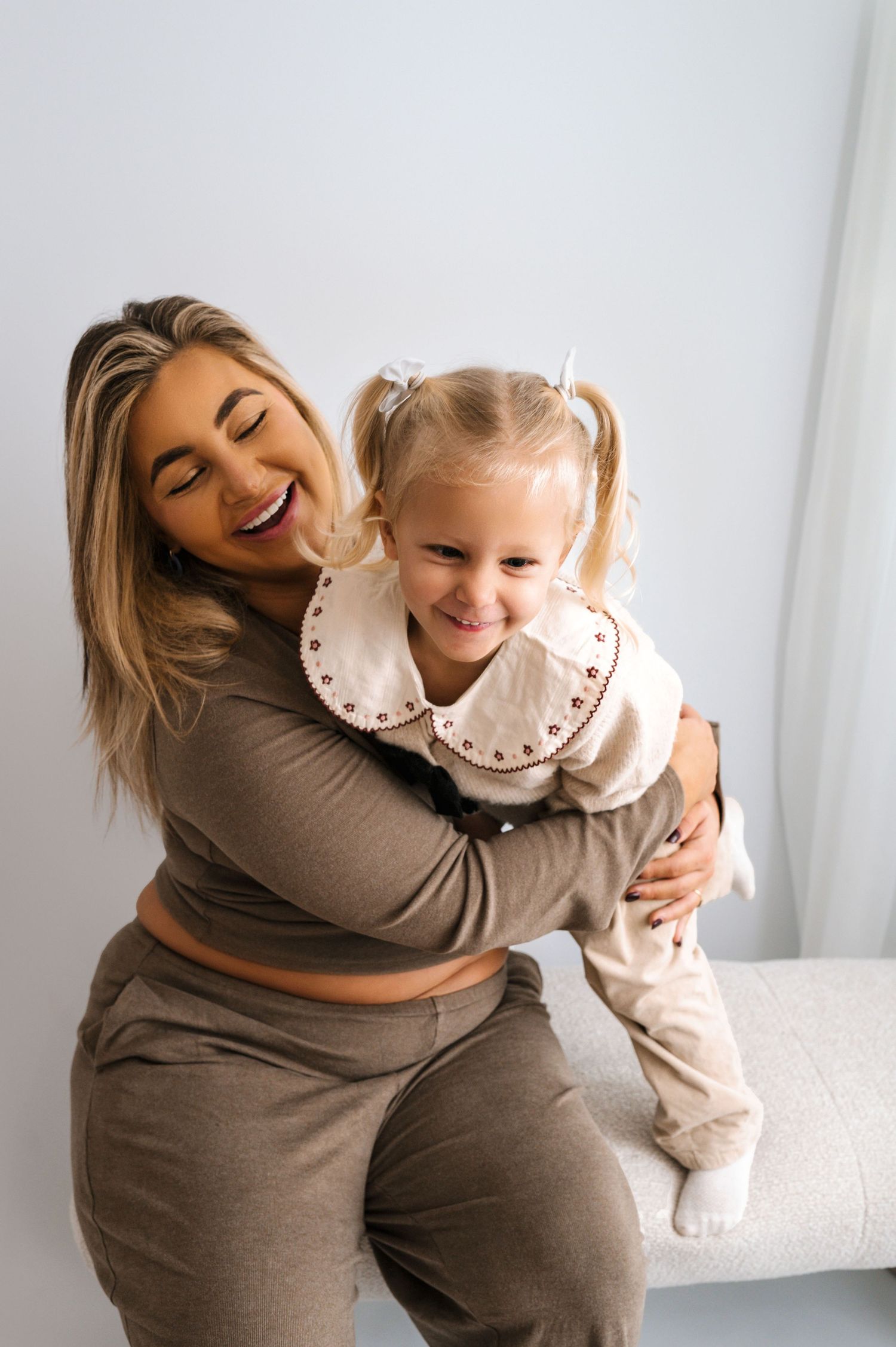 A joyful candid moment between parent and child laughing and embracing on a white couch.