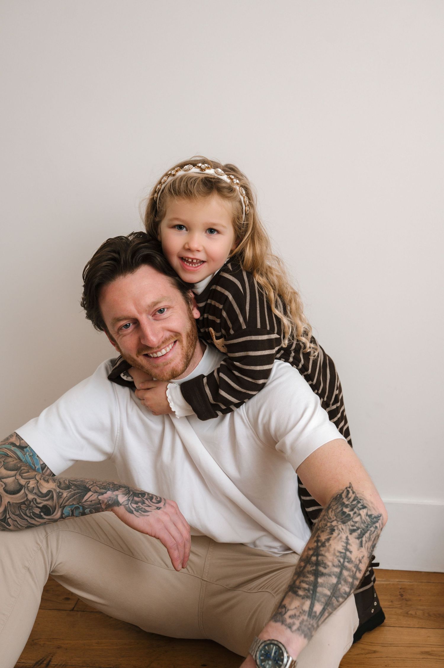 A sequence of casual portrait photos showing a person in a white t-shirt with arm tattoos posing against a light wall.