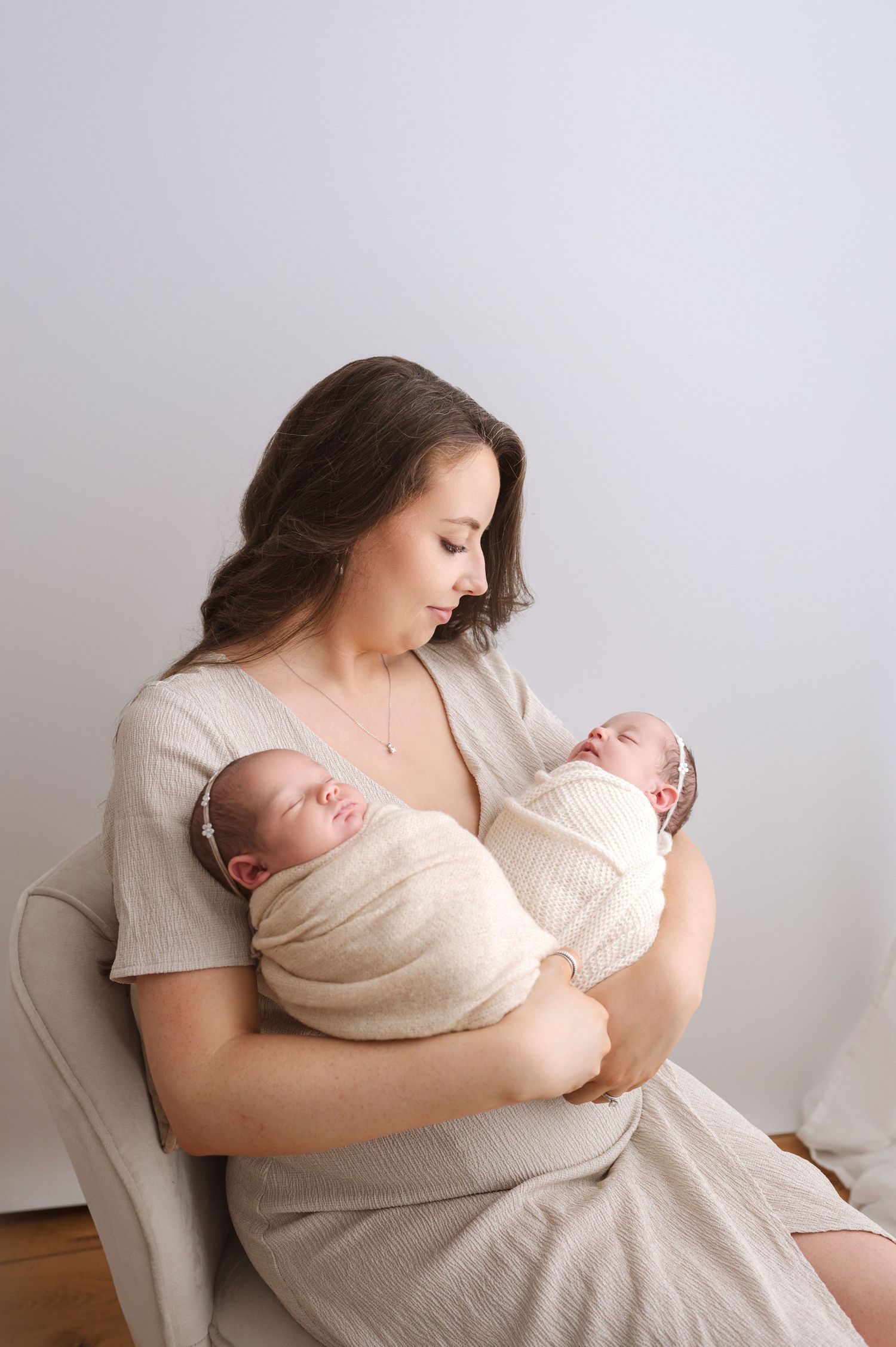 A mother in a white shirt tenderly holds and nurses her newborn baby in a minimalist setting.