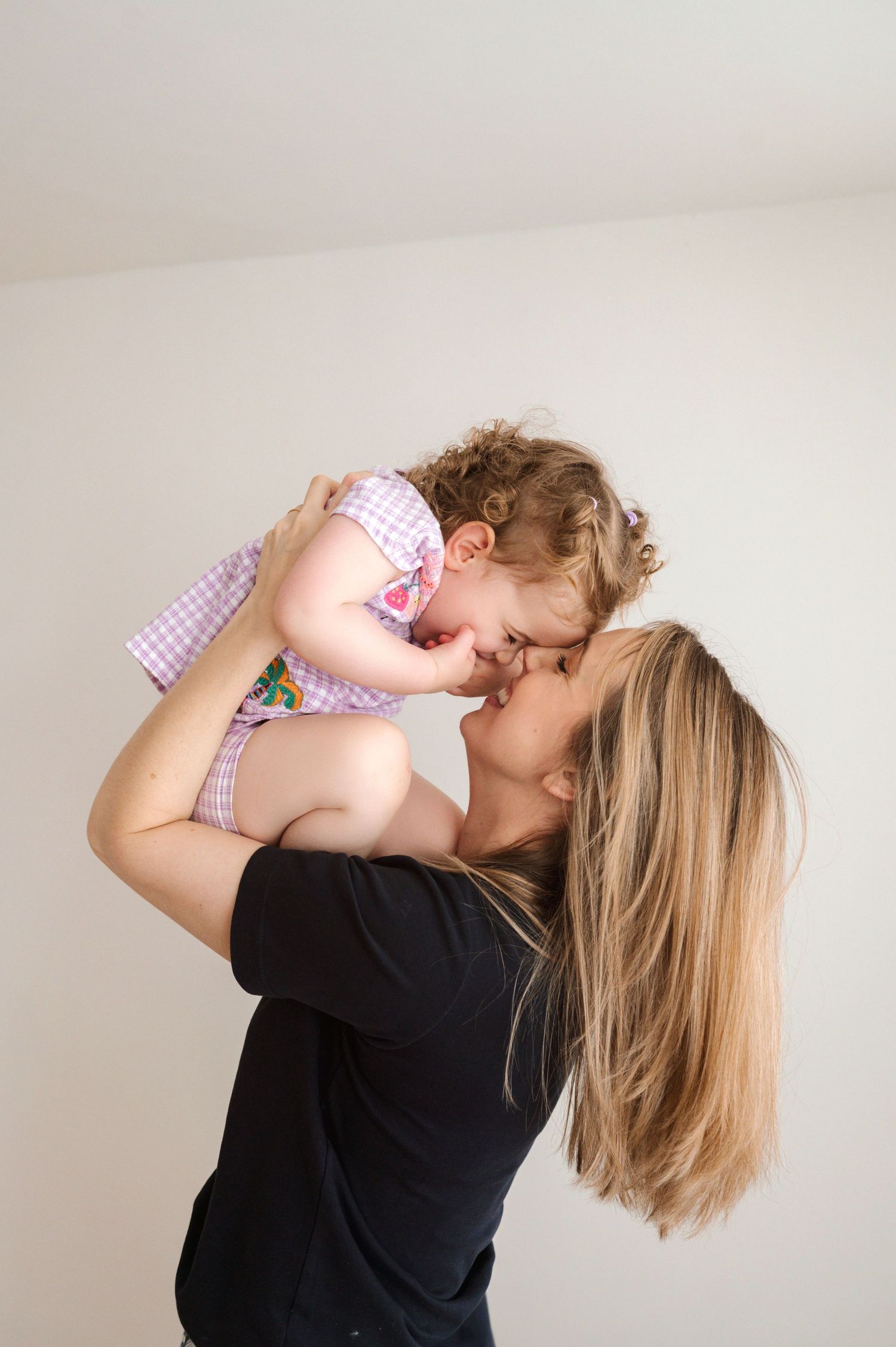 A tender moment shared between parent and baby in matching pink gingham outfits against a neutral wall.