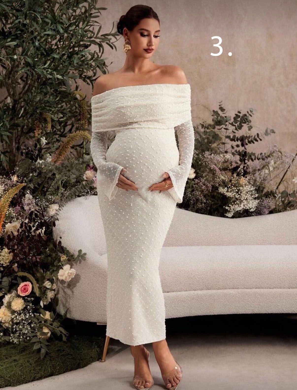 Elegant off-shoulder white maternity dress with textured fabric and long sleeves, styled with floral backdrop.