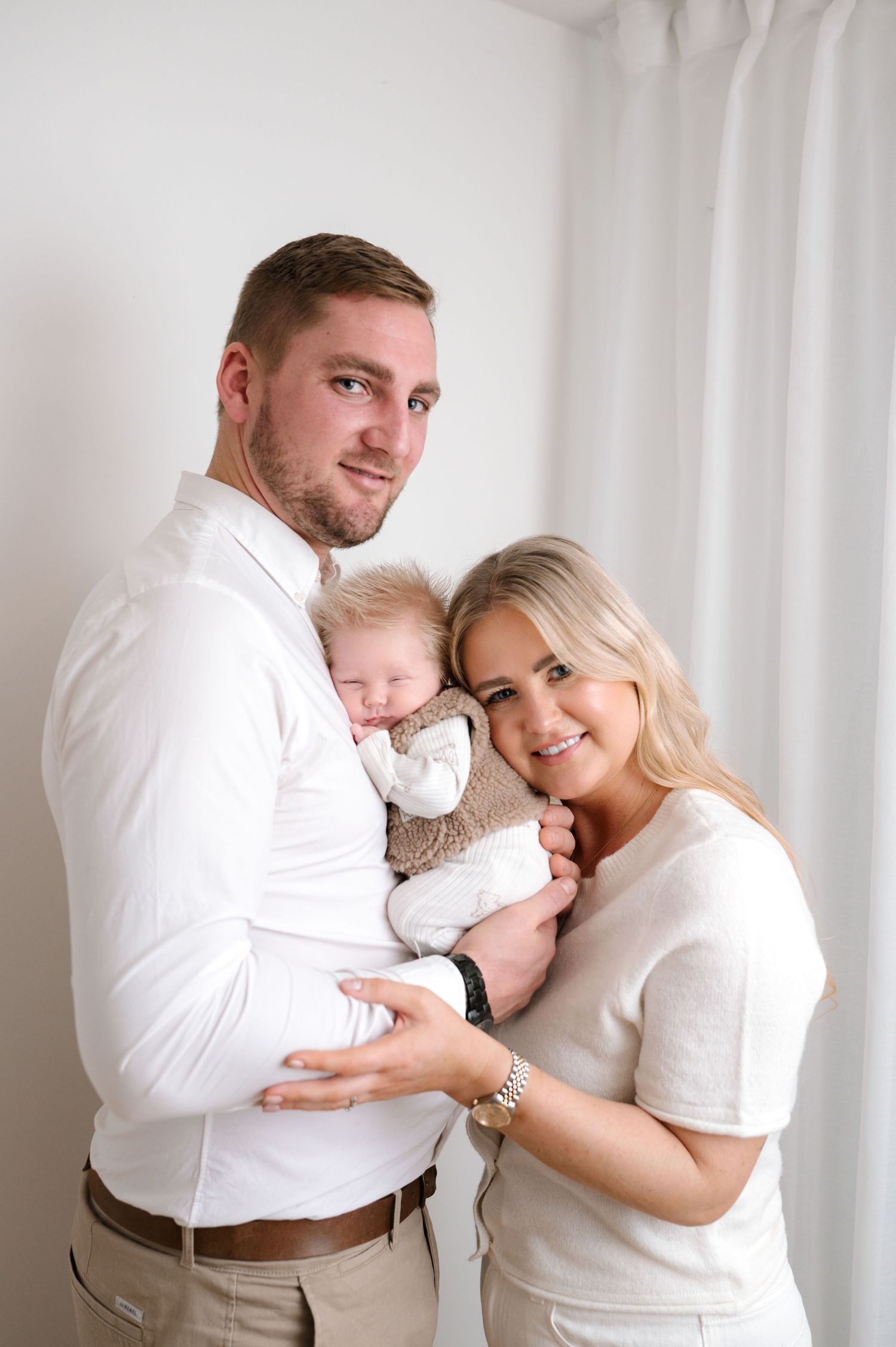 A family wearing white outfits embraces tenderly in a bright studio setting across multiple intimate poses.
