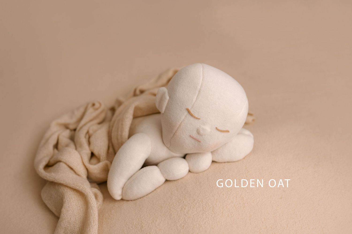 Peaceful sleeping newborn baby sculpture in cream tones curled up on soft fabric with Golden Oat text overlay.