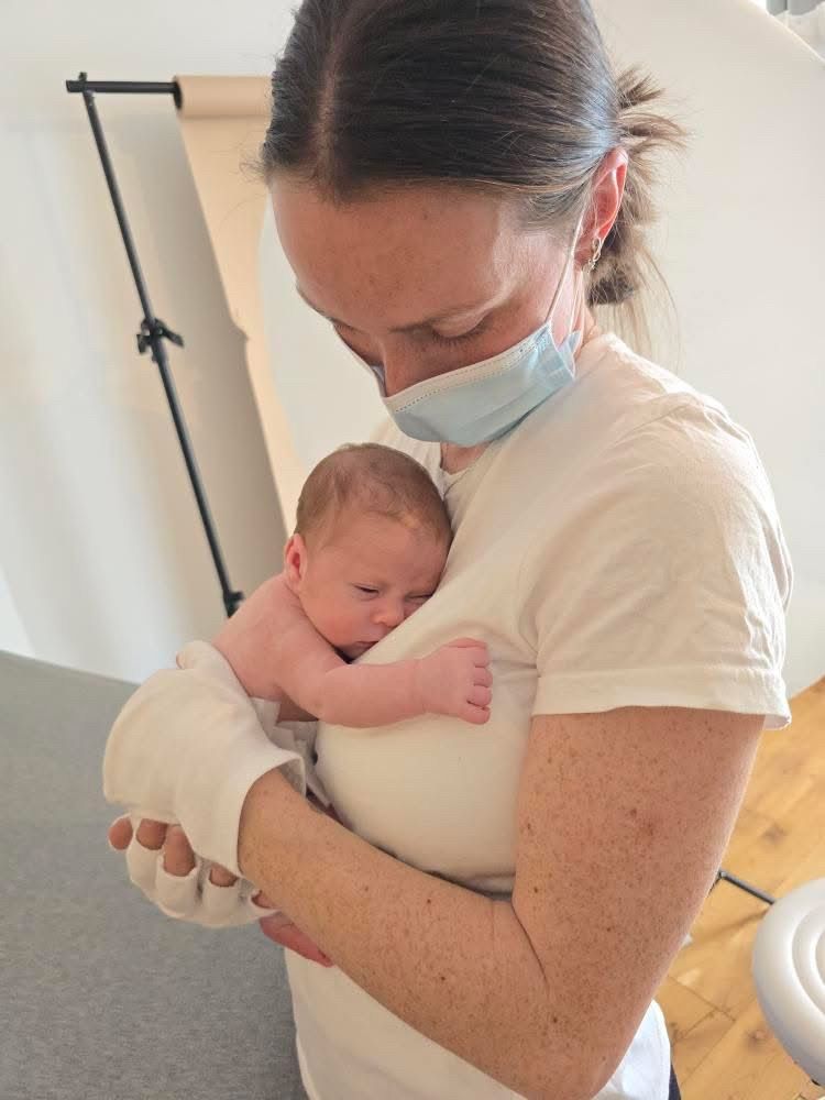 Pengelly Portraits wearing protective face mask holds and comforts newborn baby in Shaldon Studio