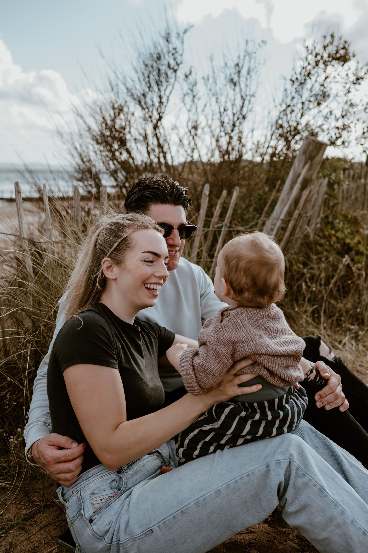 A family shares joyful moments together while sitting outdoors in nature during a casual photo session.