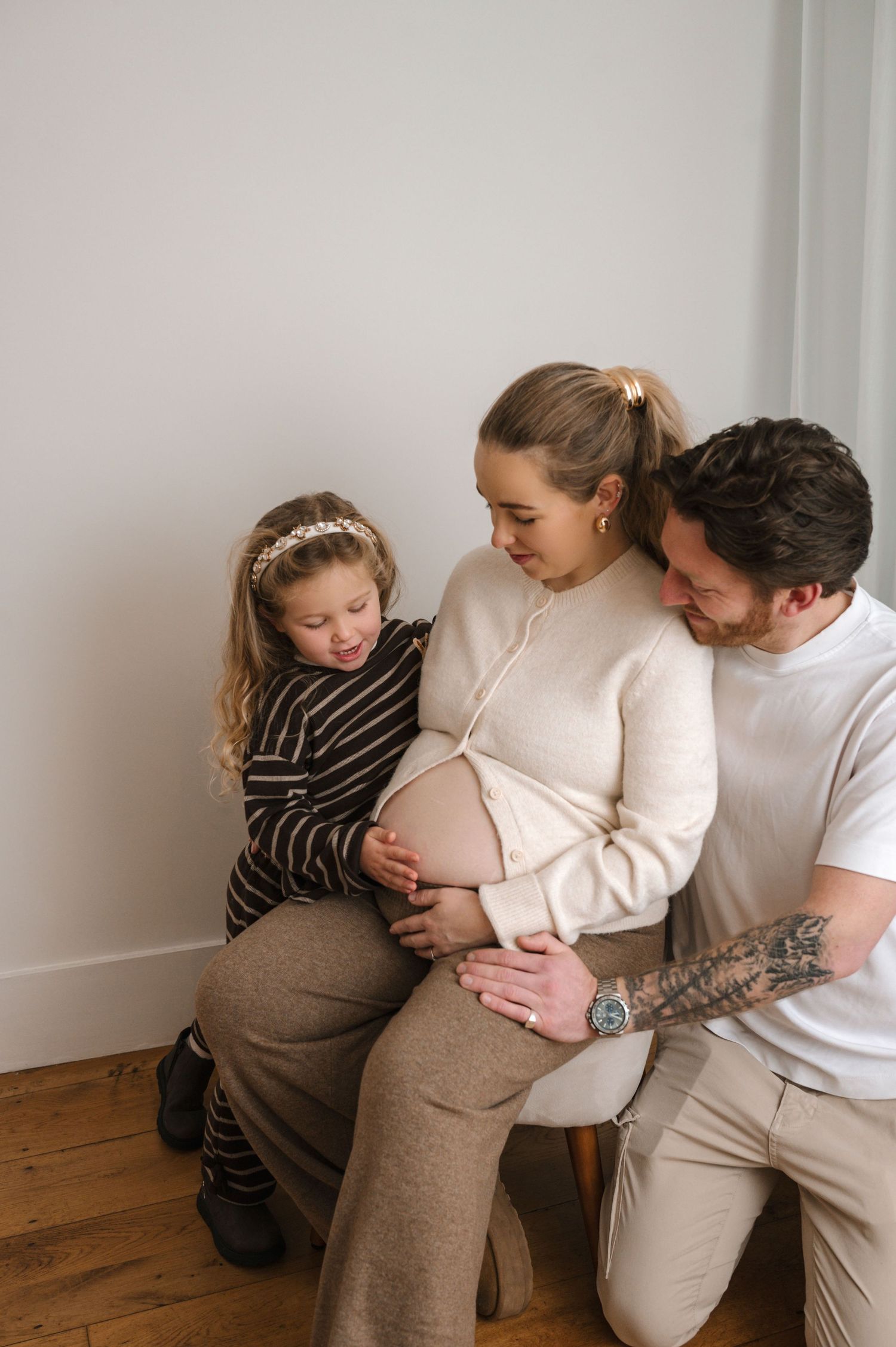 A series of four intimate maternity photos showing a couple embracing against a white wall with wooden floors.