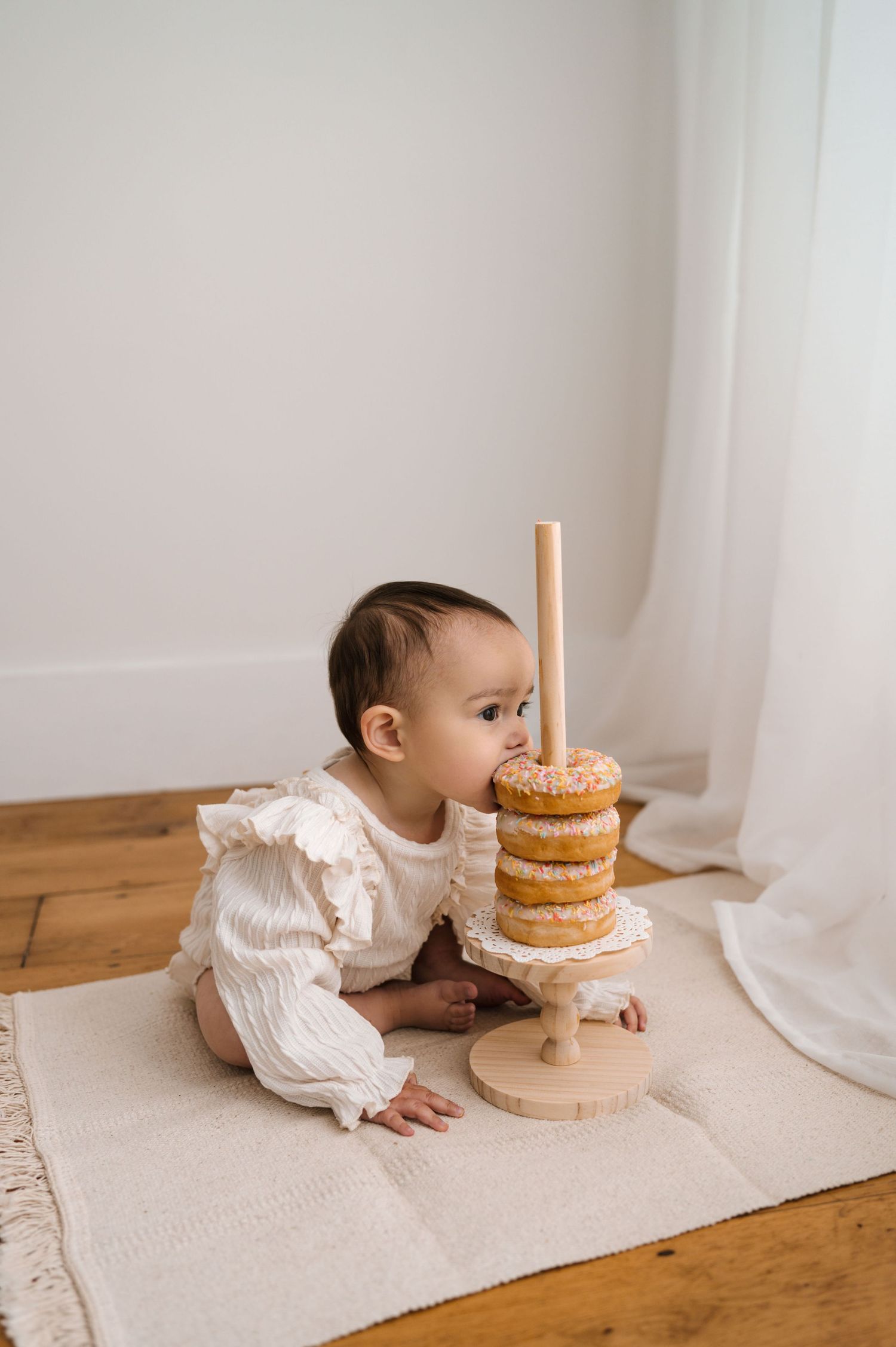 A sequence of photos showing a baby crawling toward a stacked donut cake on a wooden floor near white curtains.