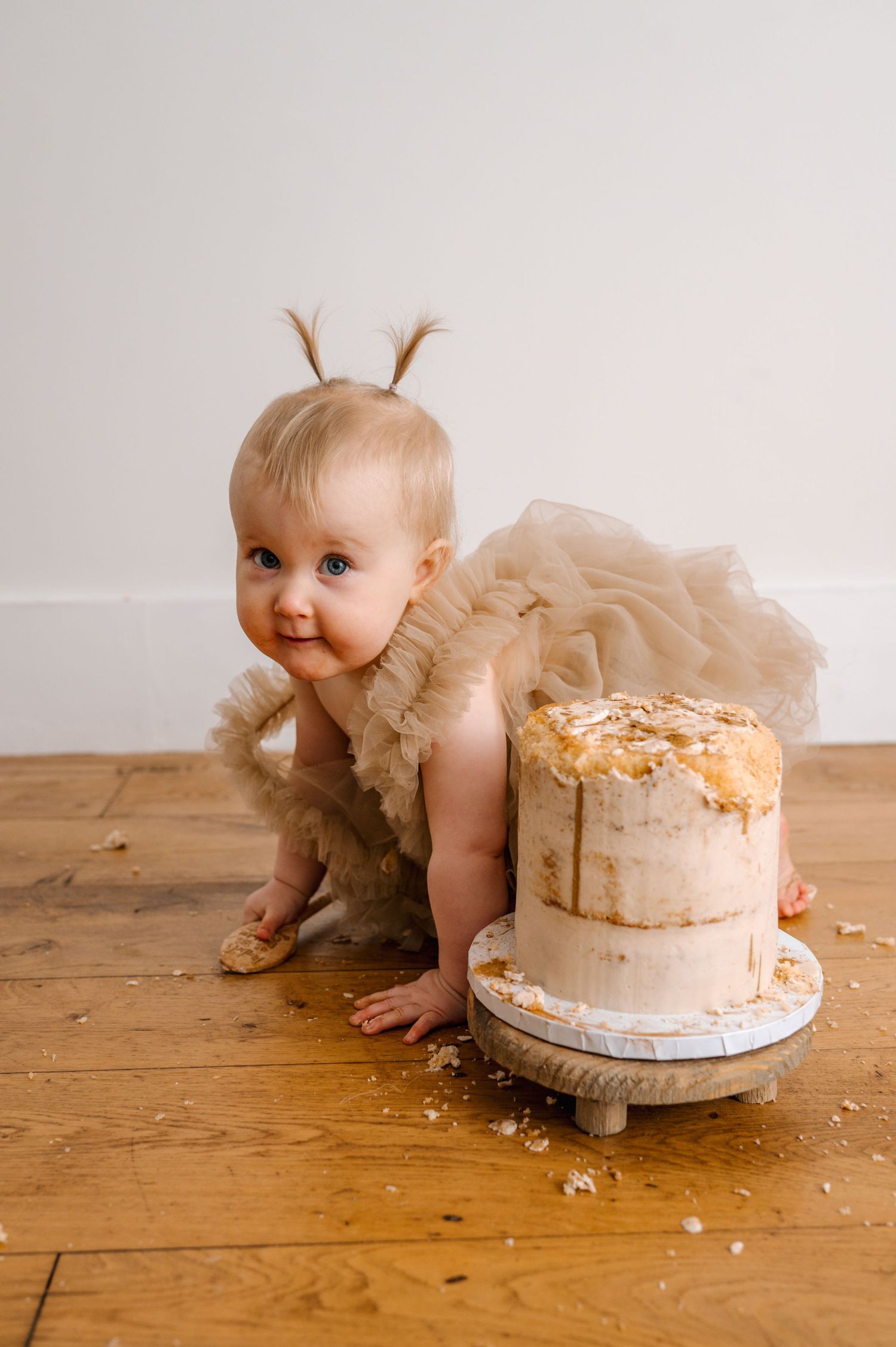 Baby girl in tutu smashes first birthday cake on wooden floor.