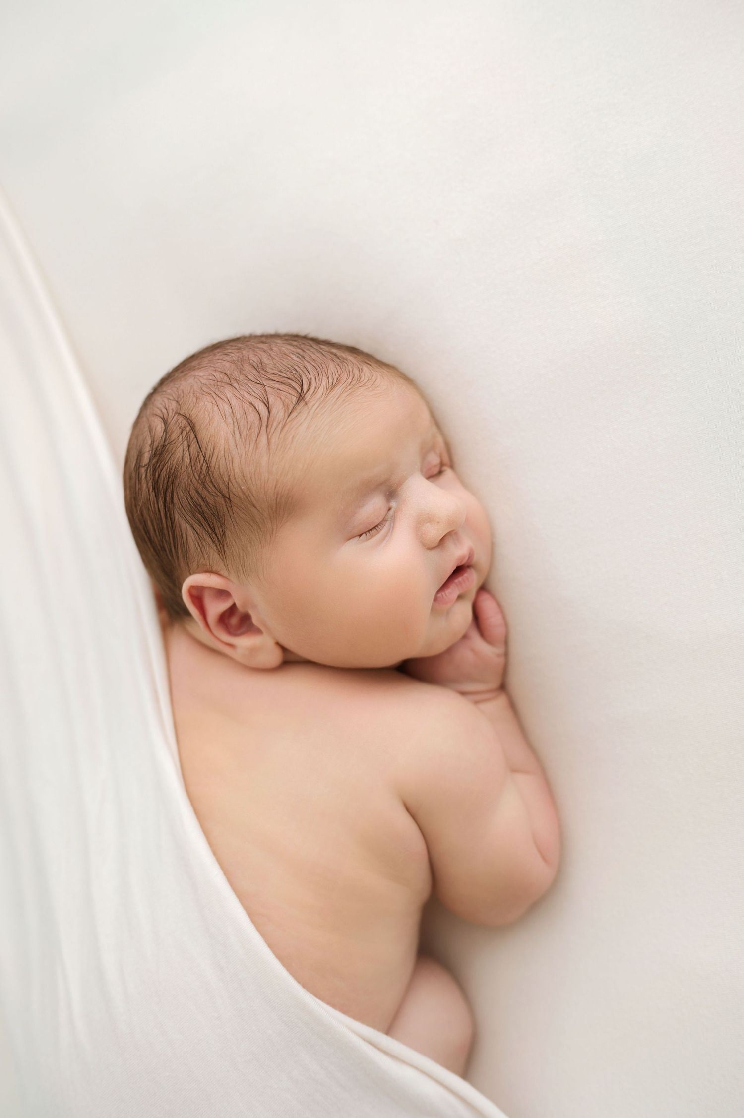 Peaceful newborn baby sleeping on white fabric wrap in a professional studio photography portrait.