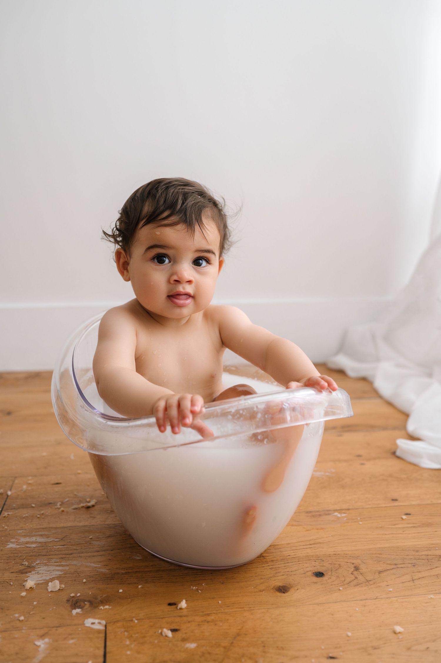 A series of progressive shots showing a small child bathing in a white ceramic bowl on a wooden floor.