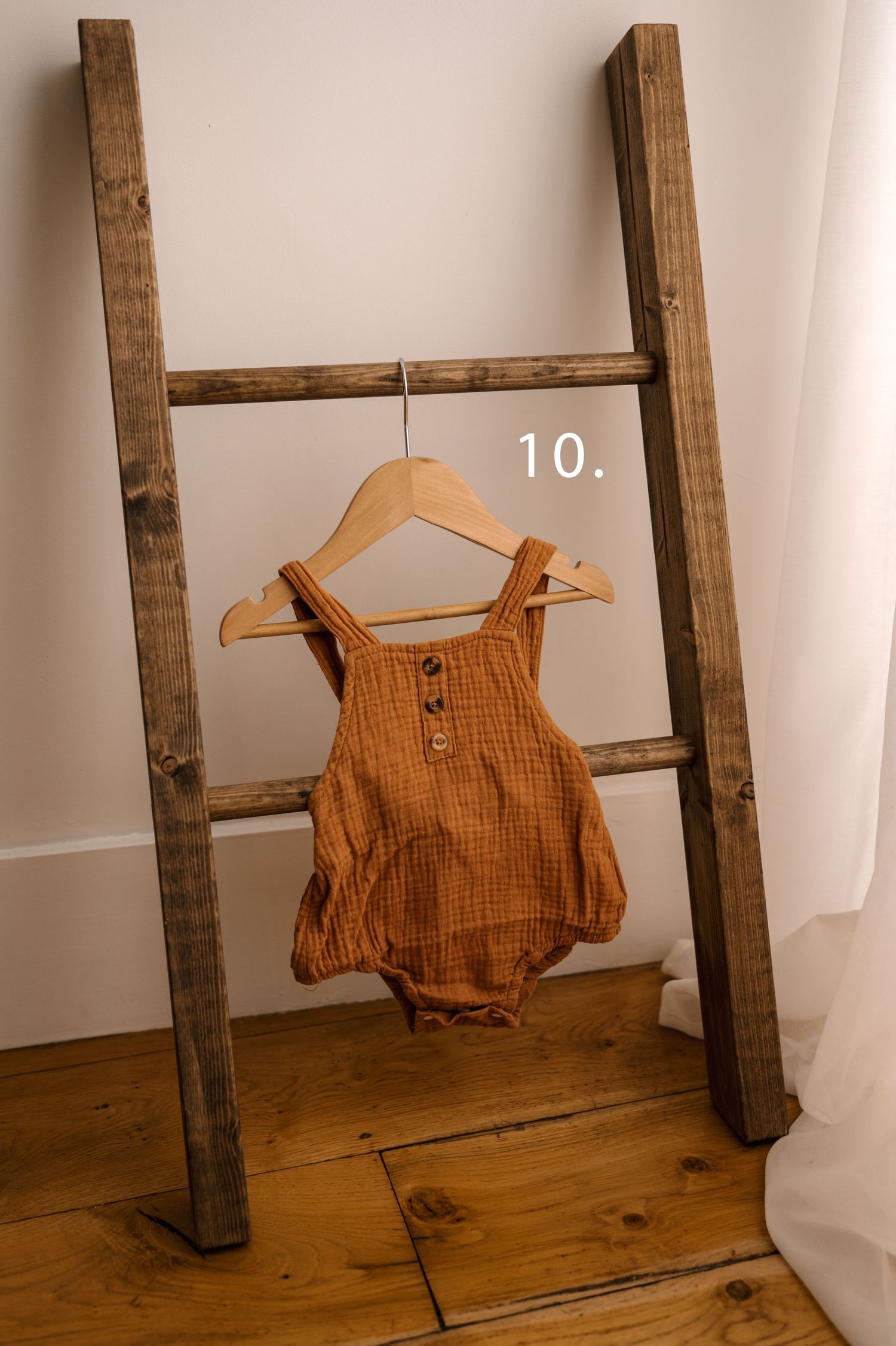 Rustic wooden ladder display with a hanging orange linen sleeveless top on a wooden hanger against a white wall.
