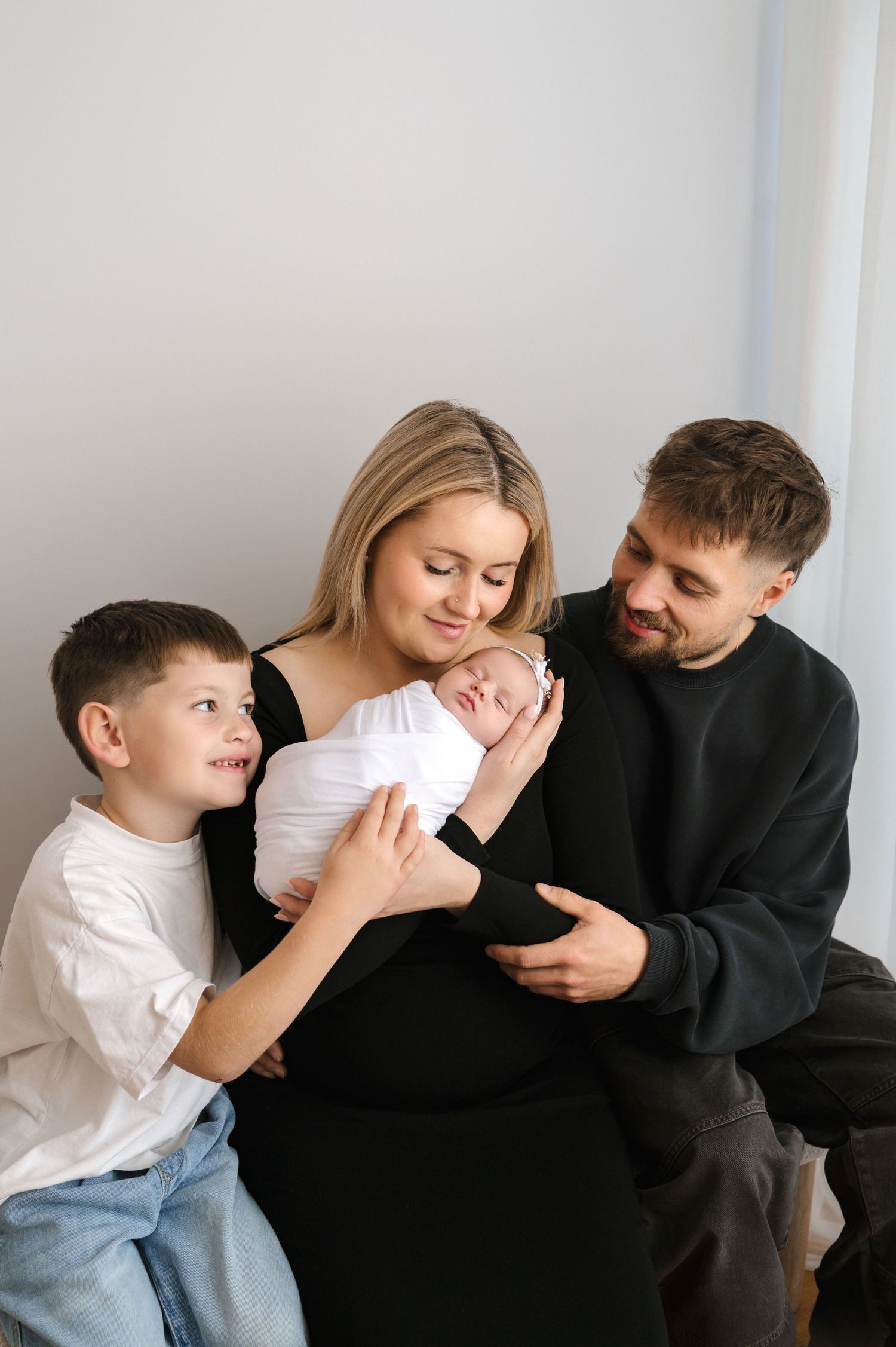 Family shares tender moment together in white room while dressed in casual black and white clothing.