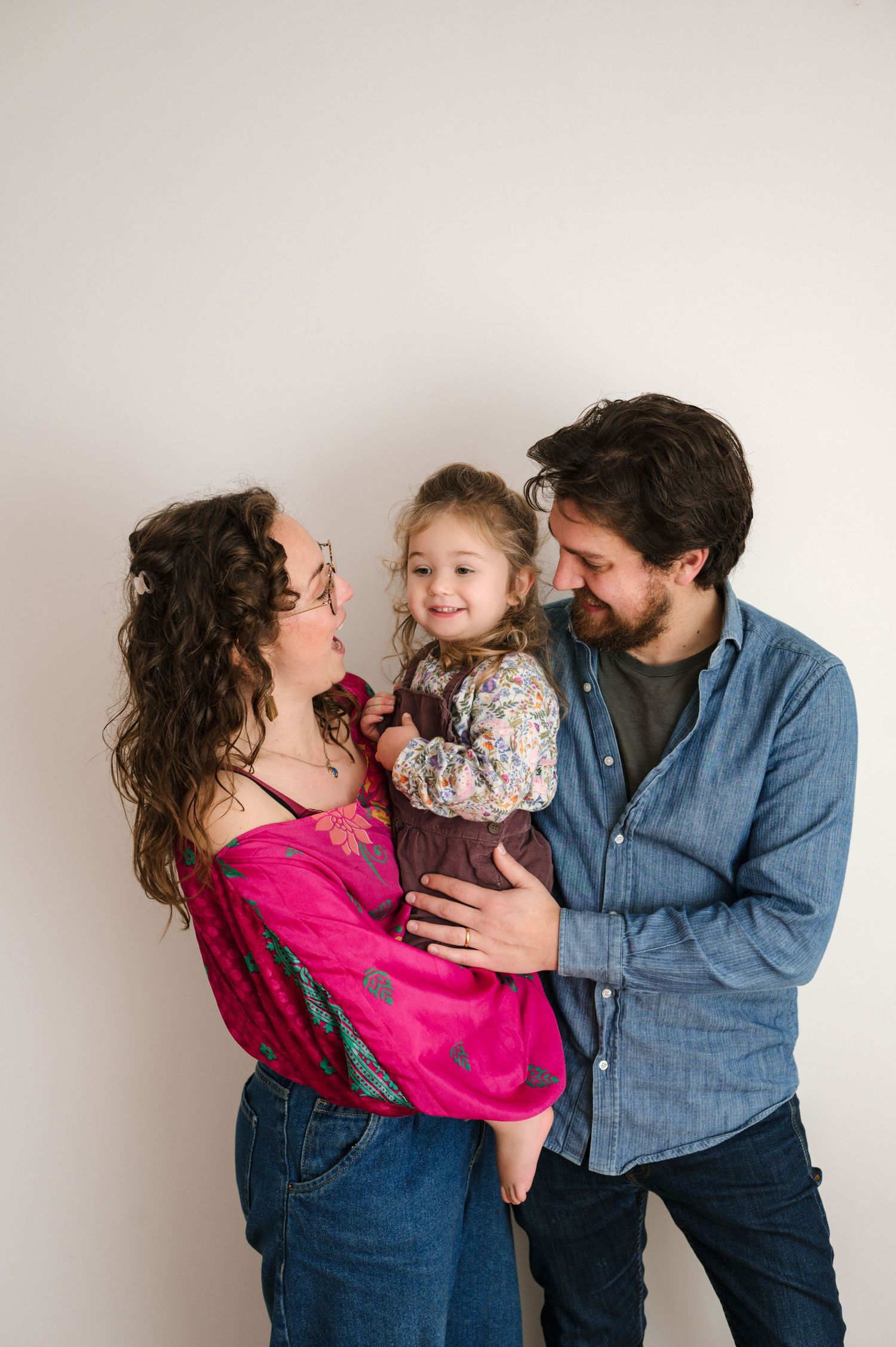 A family in matching denim and pink outfits shares playful moments in a photo series against a white backdrop.