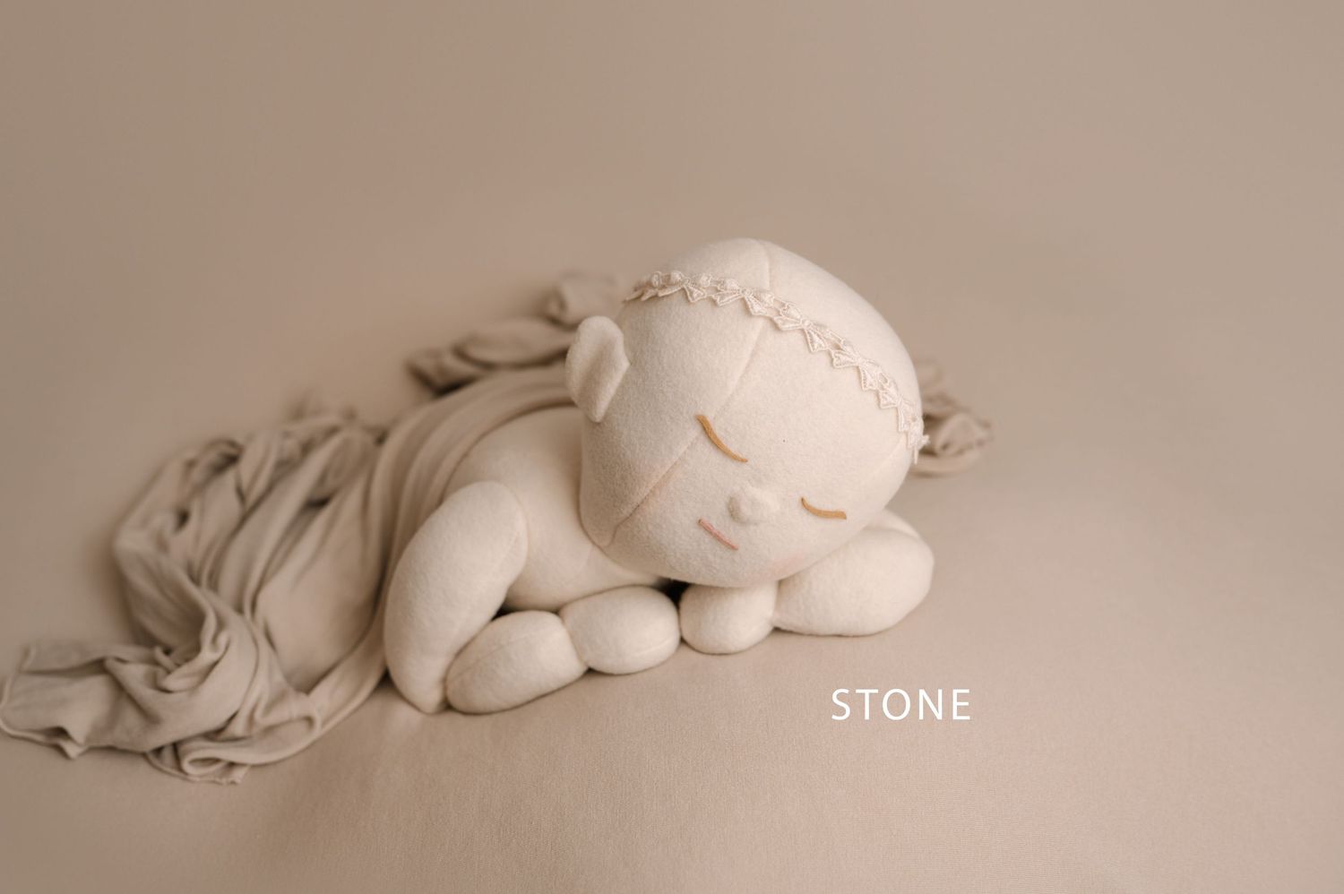 Peaceful sleeping baby sculpture in stone color wrapped in soft fabric against neutral background.