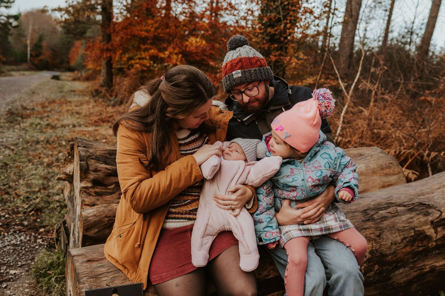 Family with two young children and a dog sitting on a log bench outdoors in autumn forest family photography at Haldon Forest.