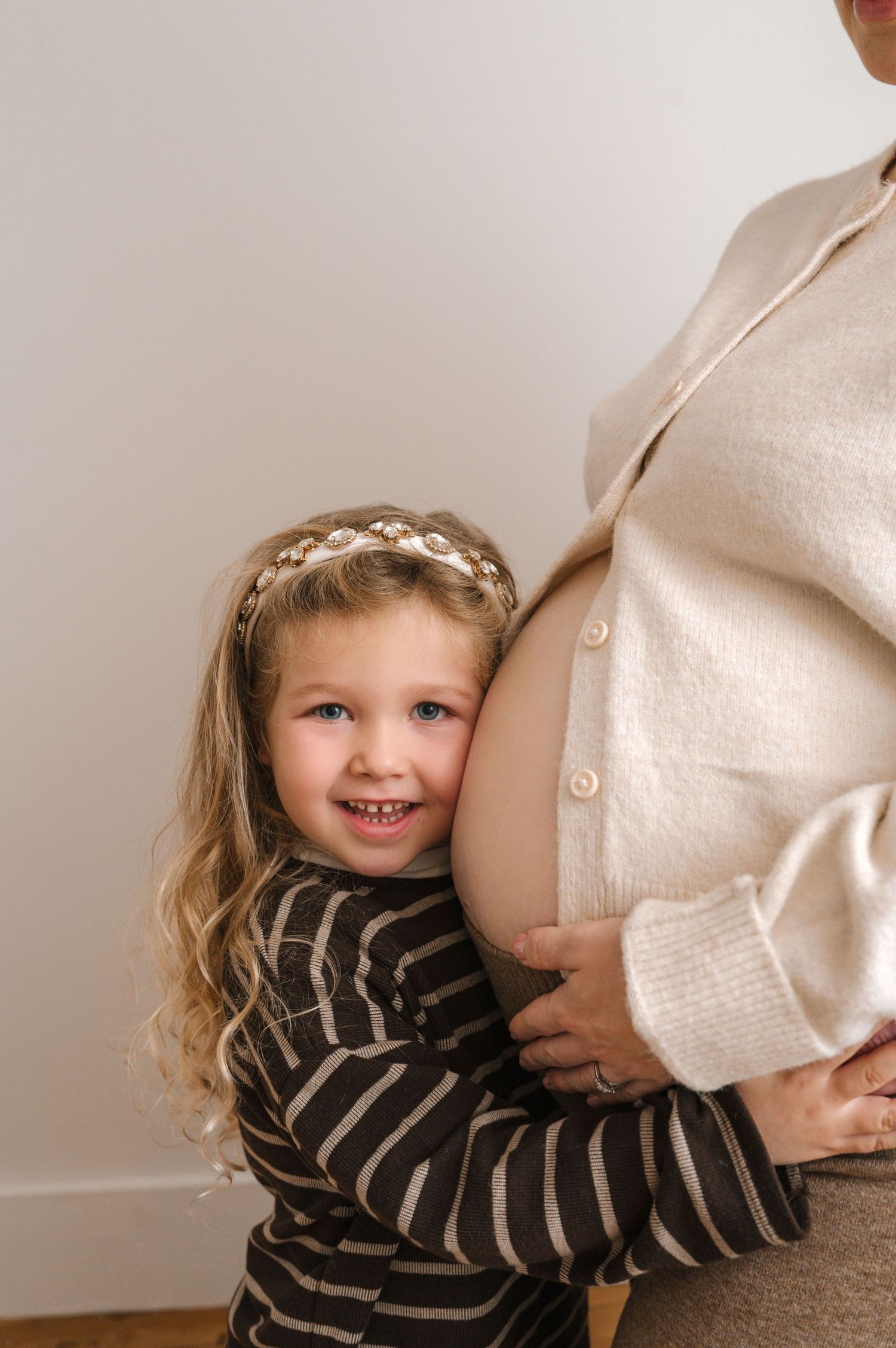 A sequence of photos showing a child in a striped shirt hugging a pregnant belly against a light background.