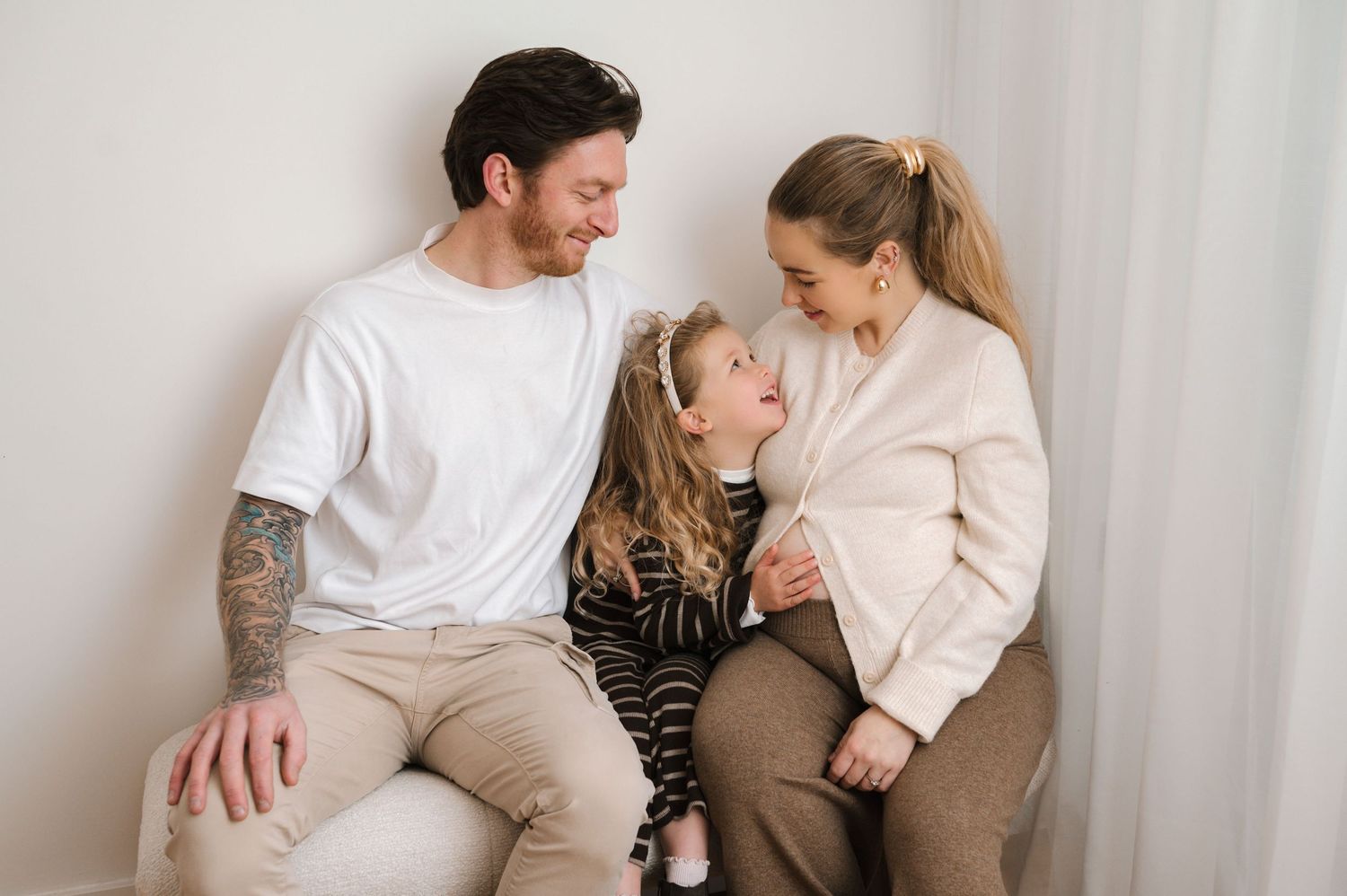 Family sitting together on a couch in coordinated neutral outfits showing affection and connection.