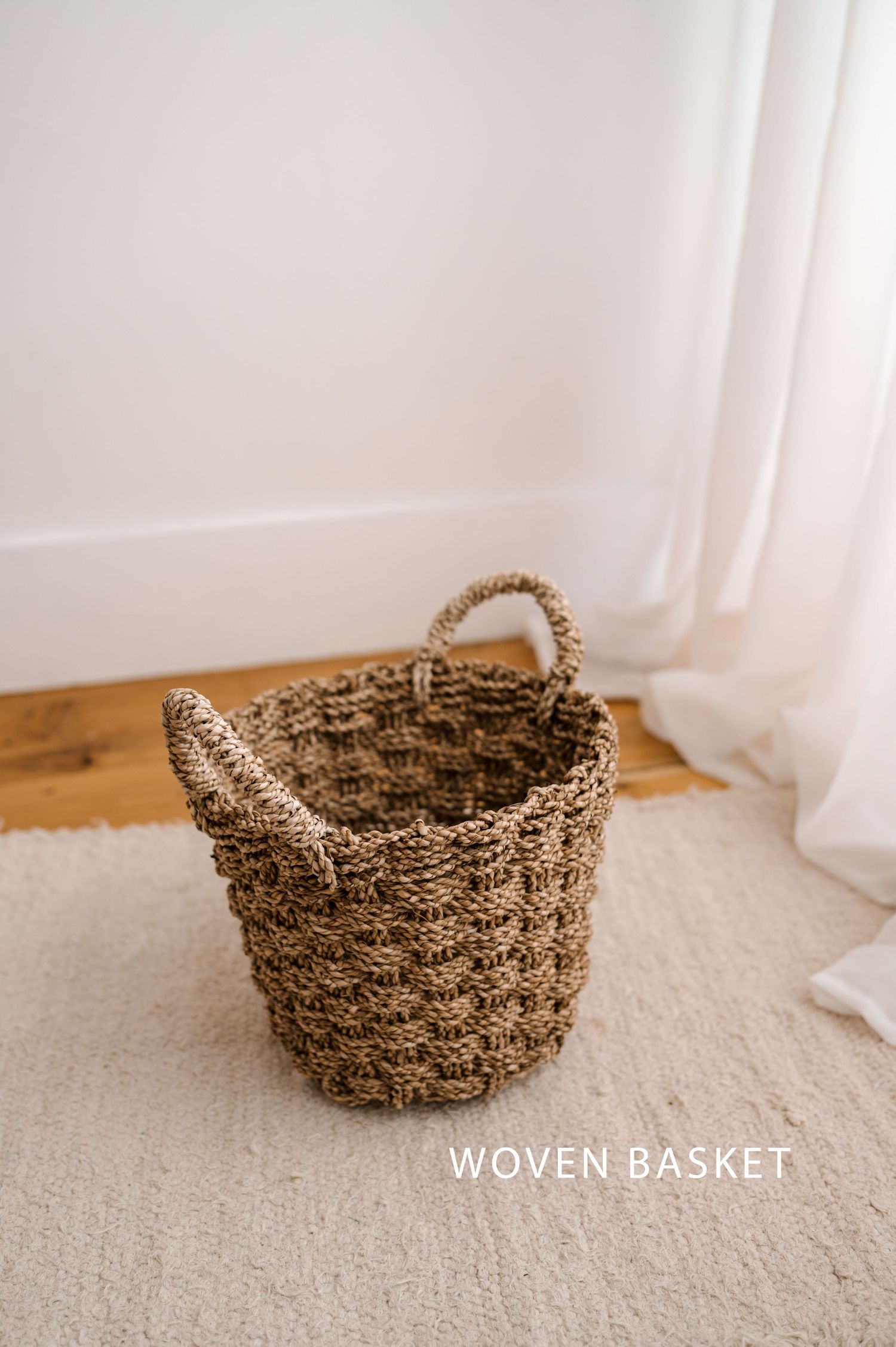 A rustic woven seagrass basket with handles photographed from multiple angles on a beige carpet near white curtains.