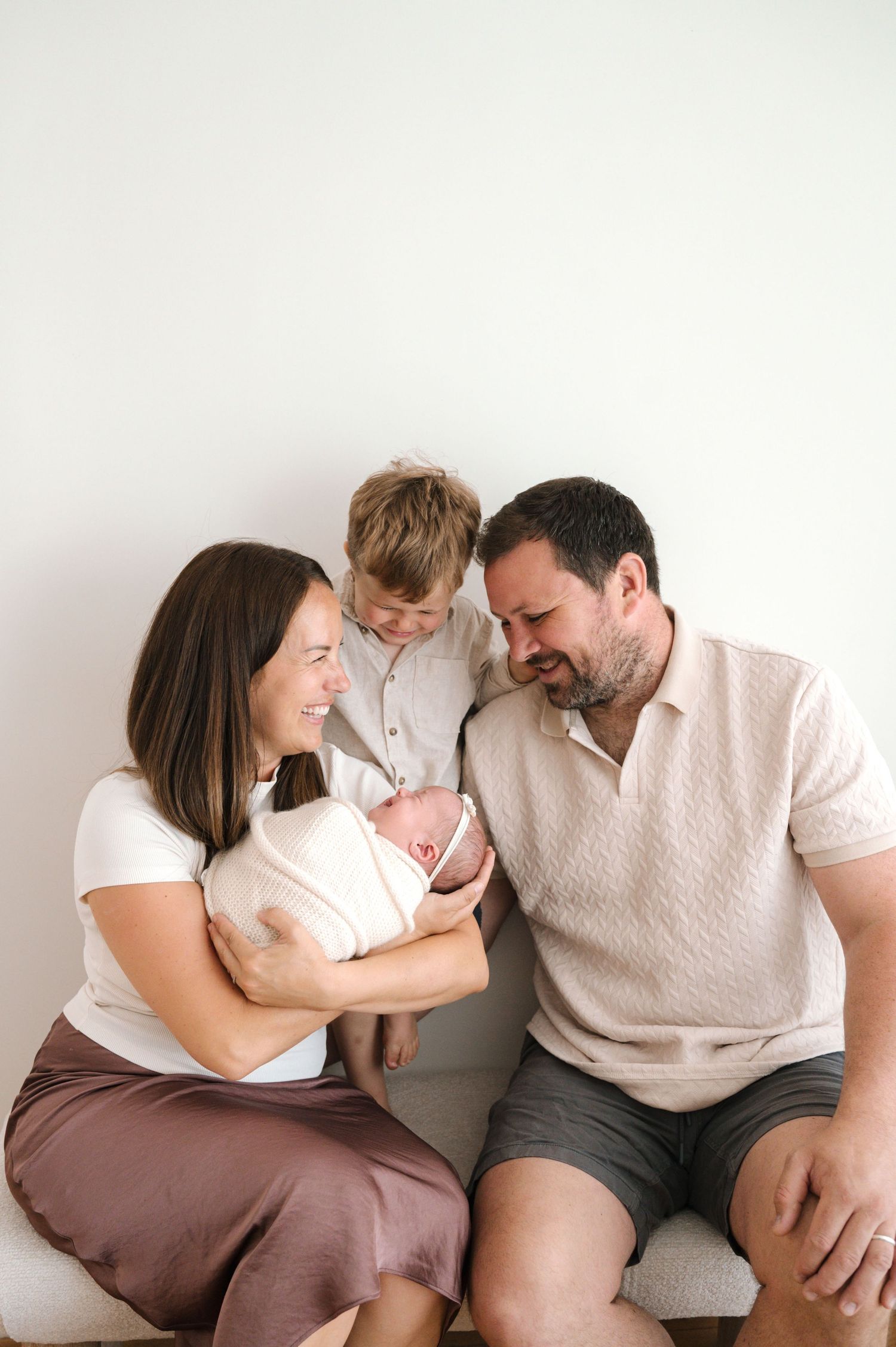 A happy family of four admires their newborn baby, with mom holding the infant while dad and young son look on lovingly.