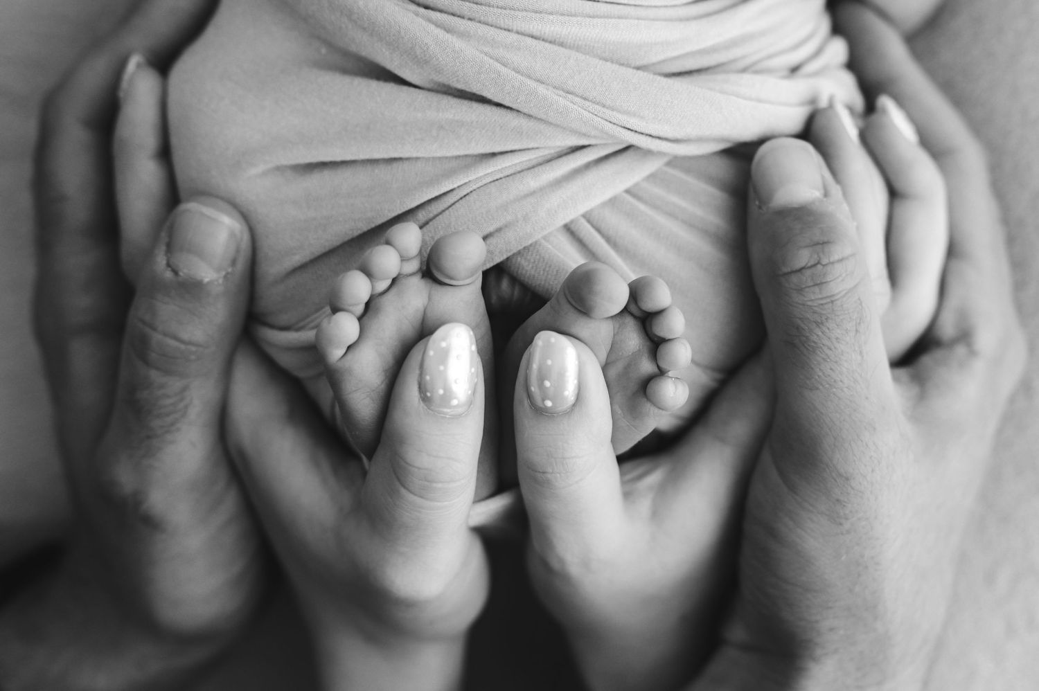 Black and white photo of newborn baby feet cradled gently in parents hands.