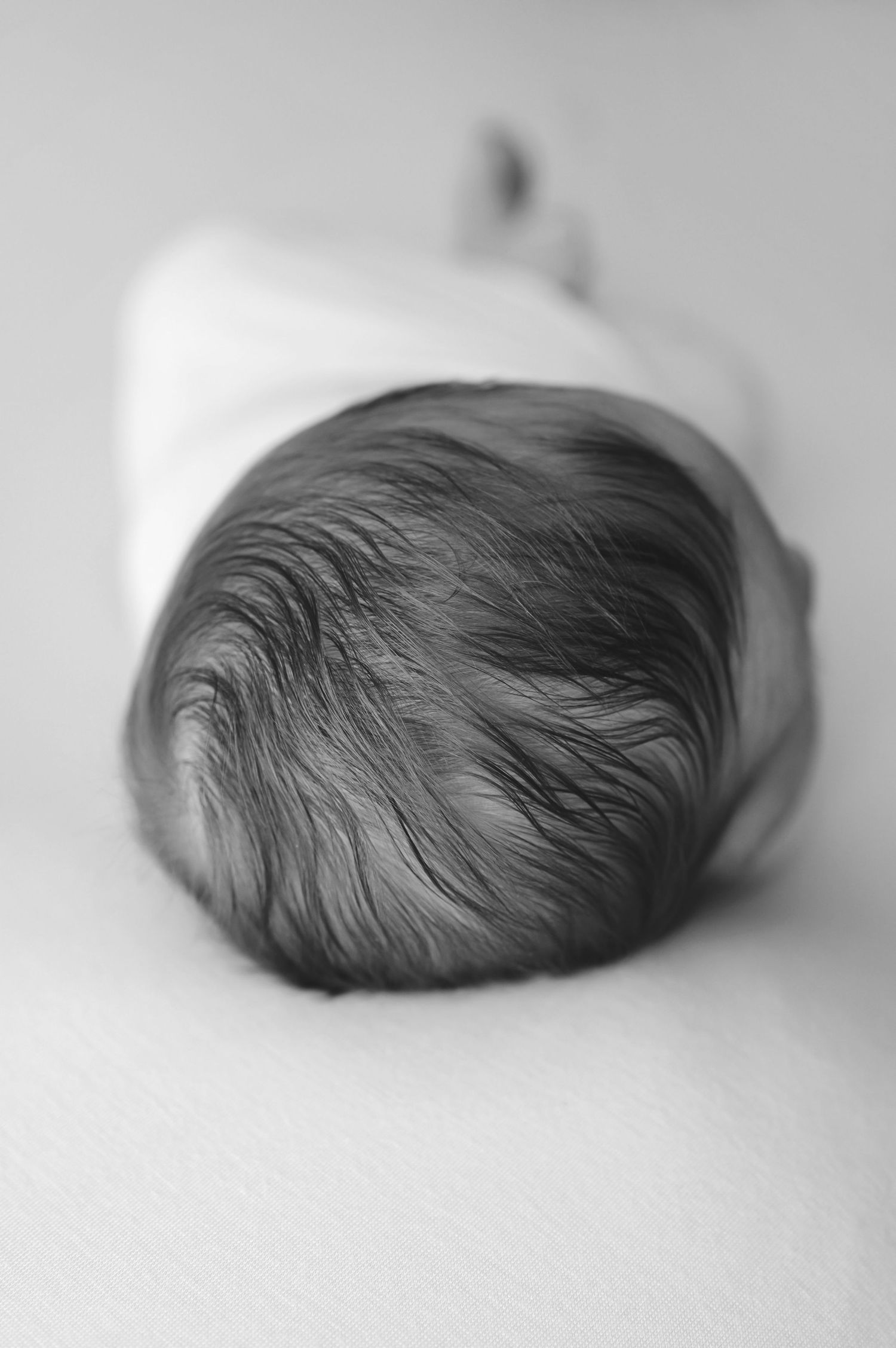 Black and white overhead view of an infant's head showing soft dark hair against a light background.