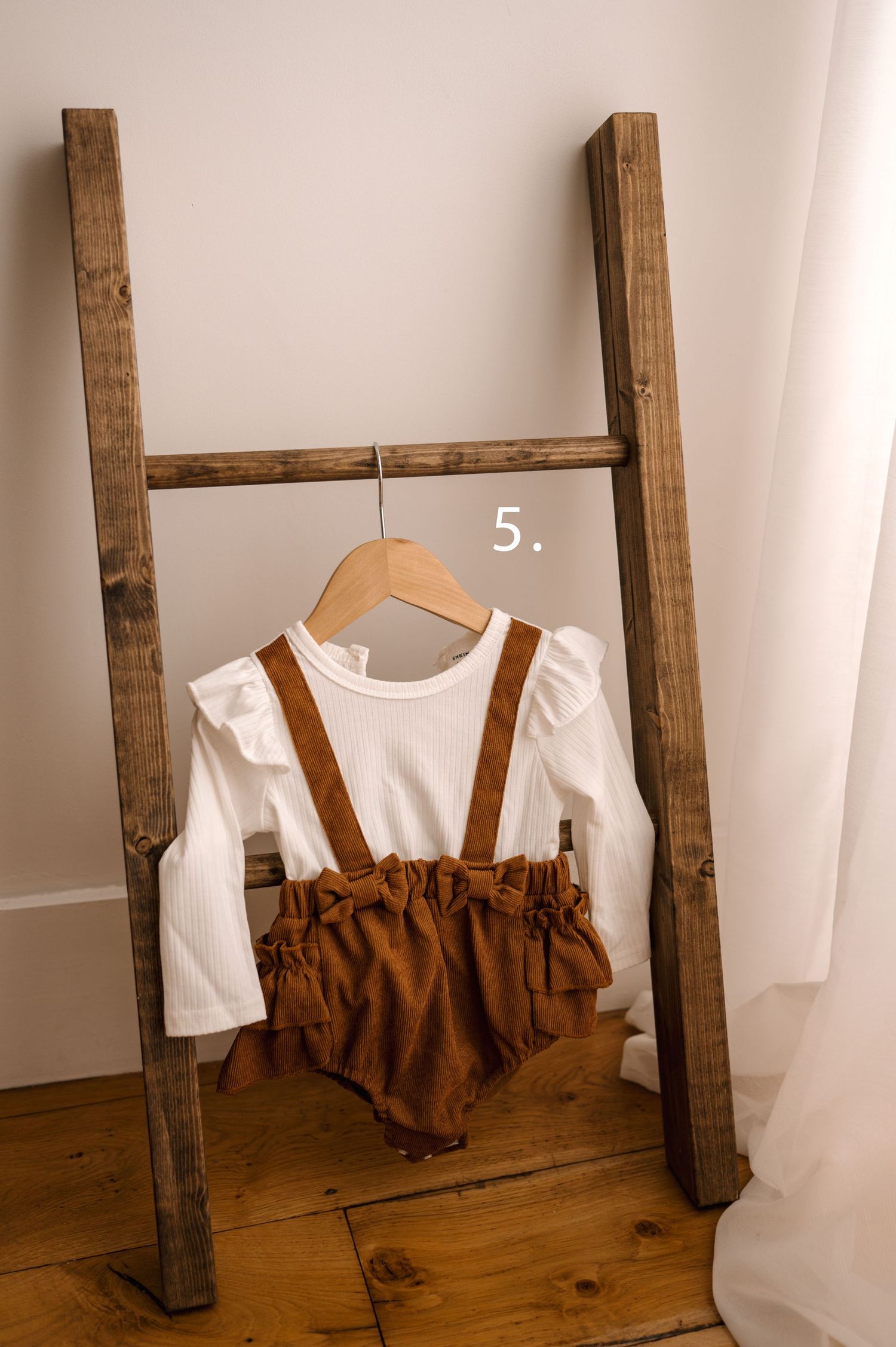 A rustic wooden ladder leans against a white wall with brown and white clothing items draped over its rungs.
