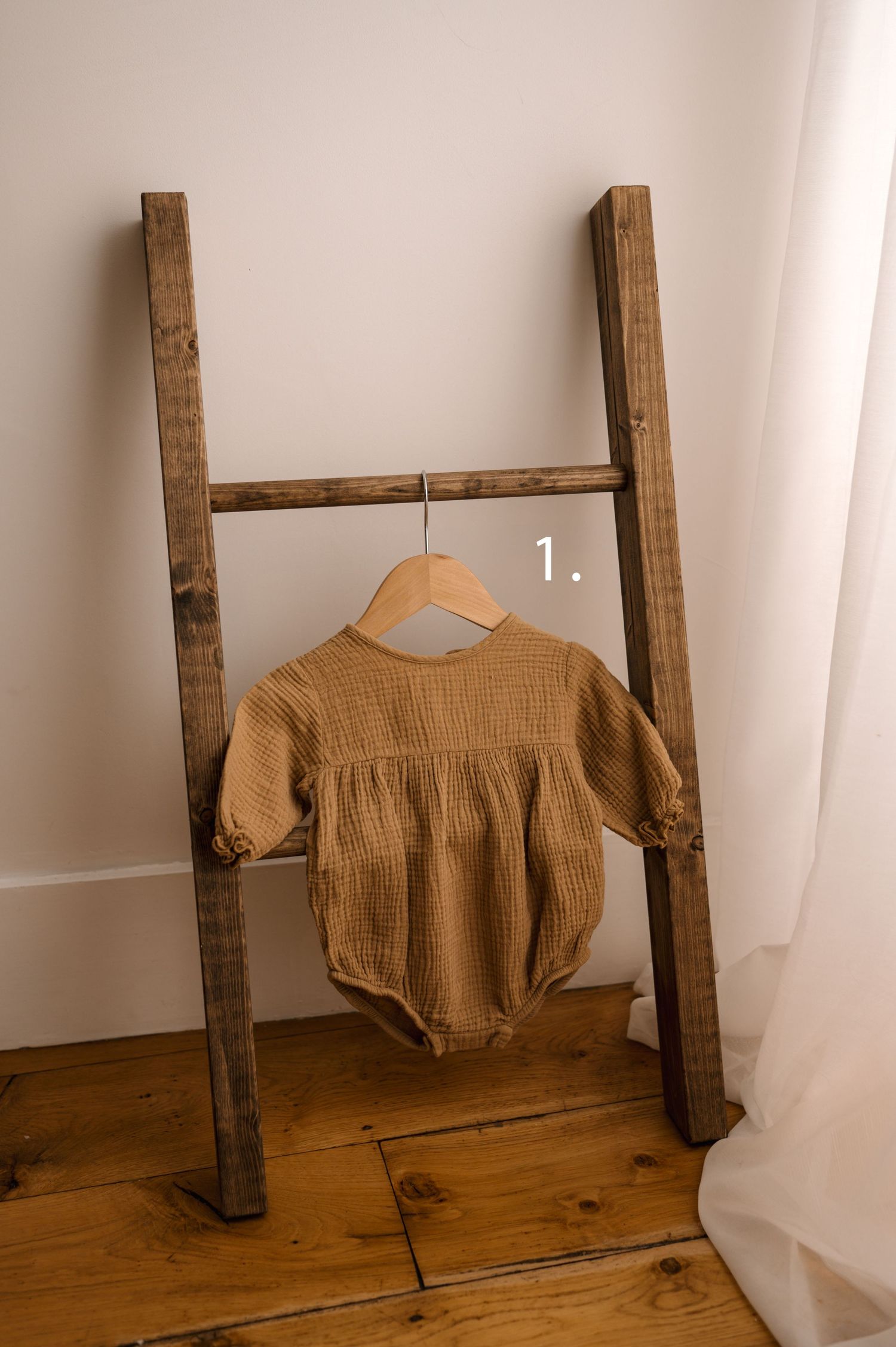 A brown garment displayed on a rustic wooden ladder-like structure against a white wall.