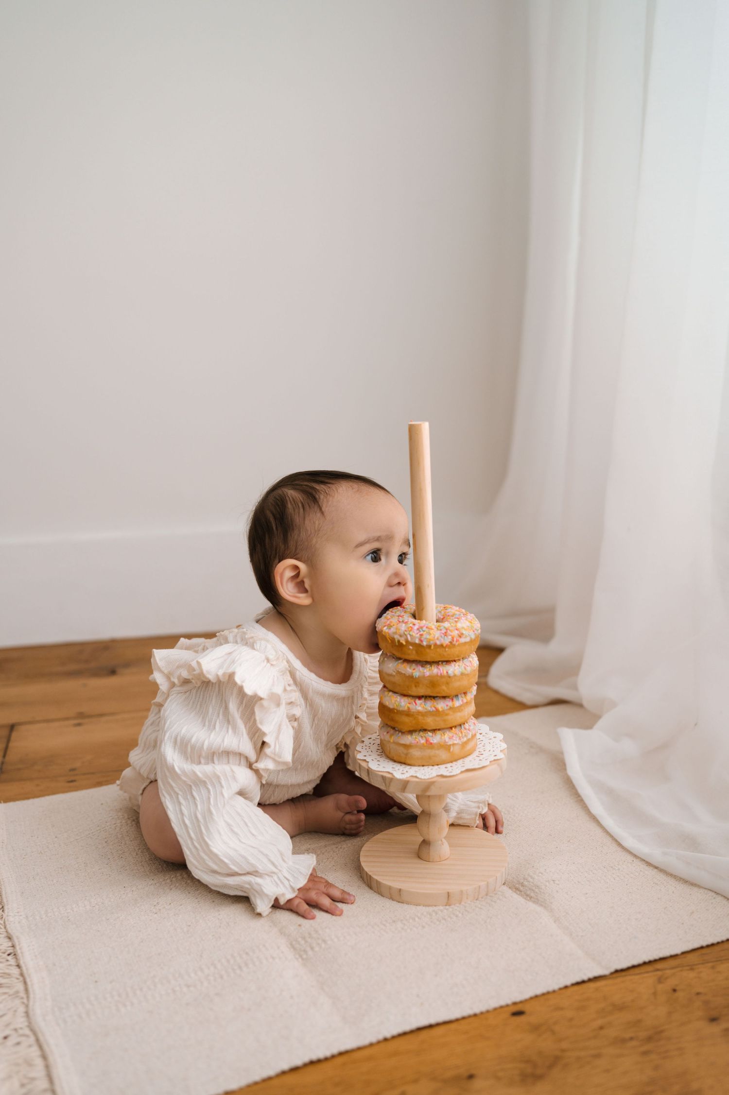 A series of photos showing a baby in white clothing crawling towards and investigating a tiered cake on a wooden floor.