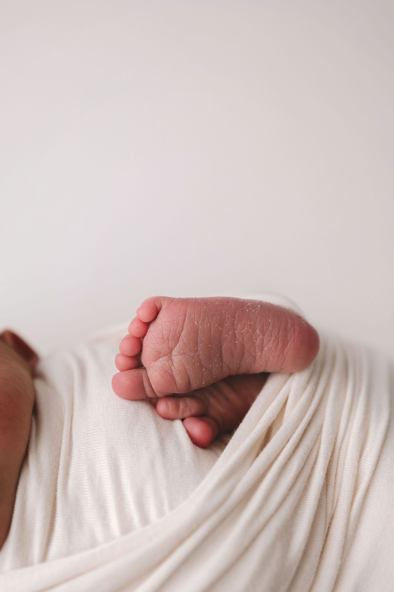 Close-up of tiny newborn baby foot wrapped in soft white fabric showing delicate toes and wrinkled skin.
