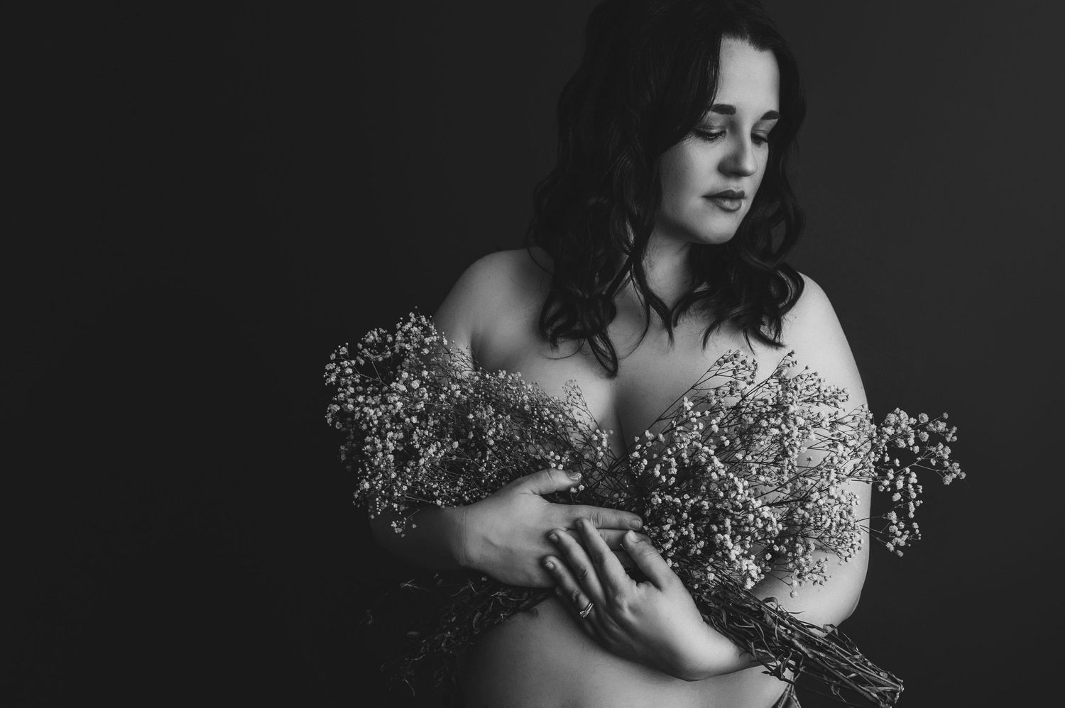 Artistic black and white portrait of pregnant mum holding delicate baby's breath flowers against bare shoulders.