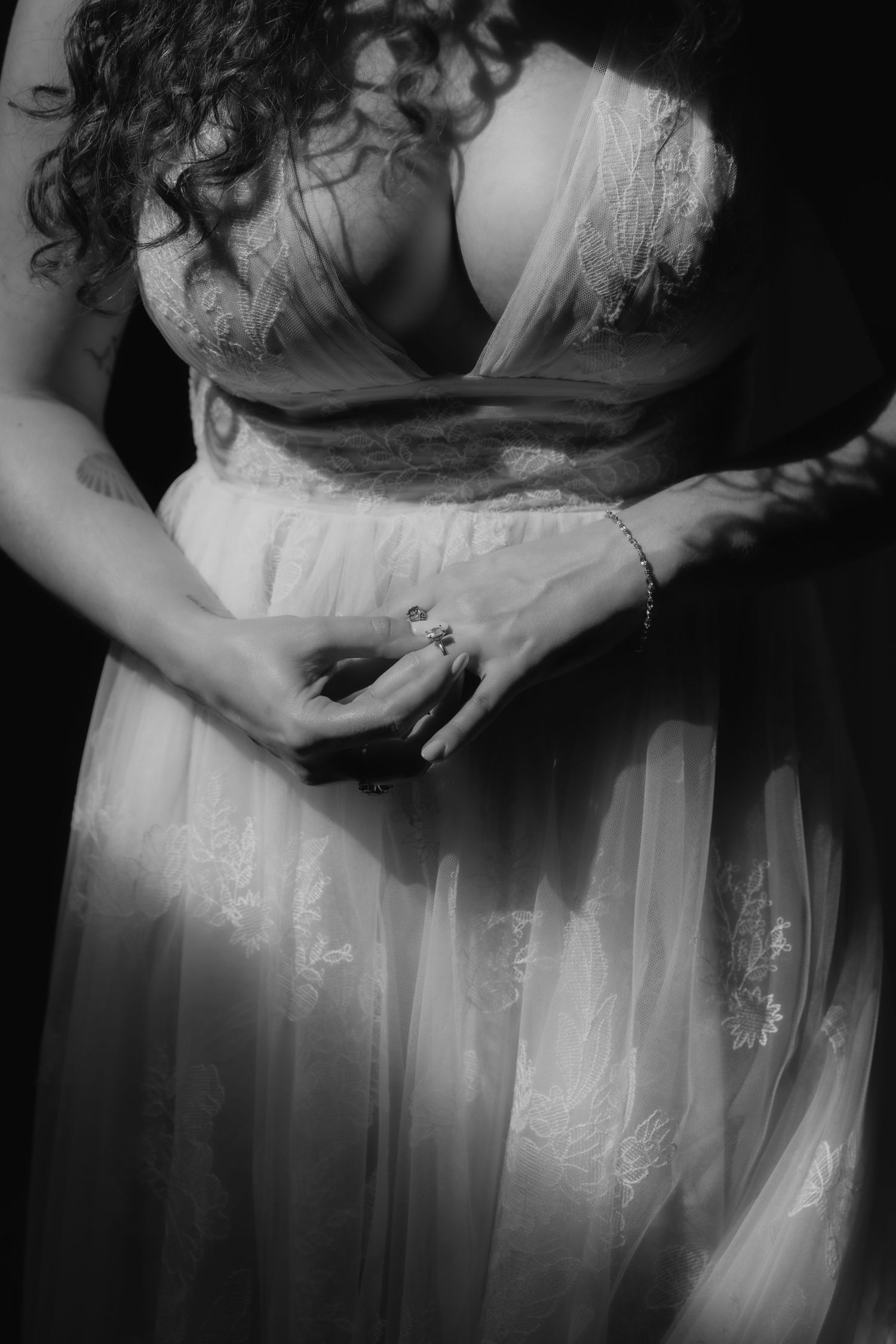 Black and white wedding photography showing details of a white lace dress with delicate embroidery patterns.