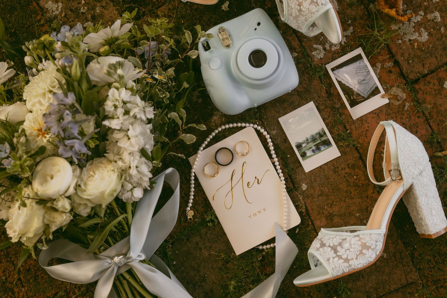 A collection of wedding details including white flowers, instant photos, and vintage-style cameras arranged on a rustic surface.