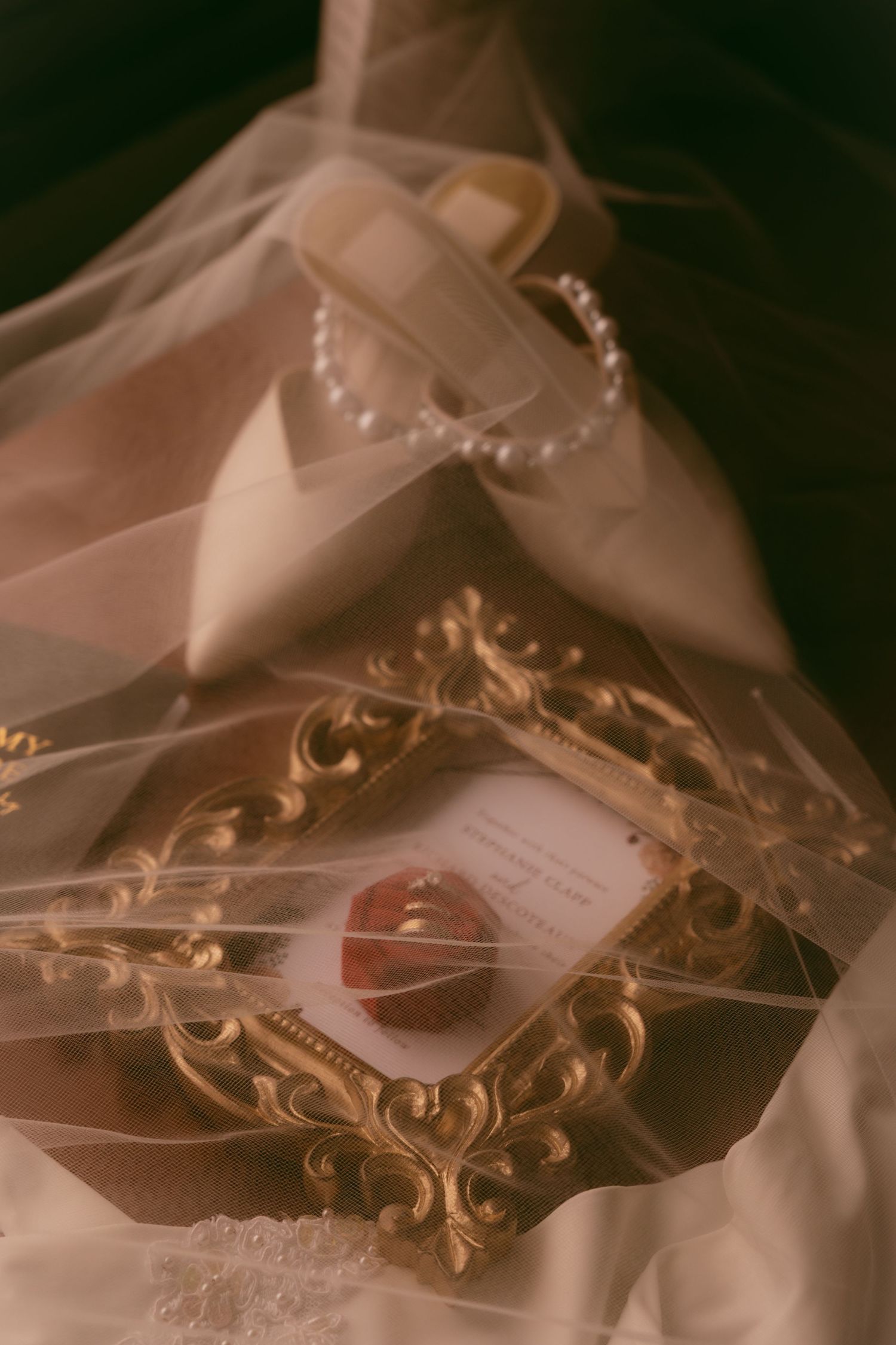 An ornate golden vintage frame with a card rests on delicate sheer fabric alongside a beaded headpiece.