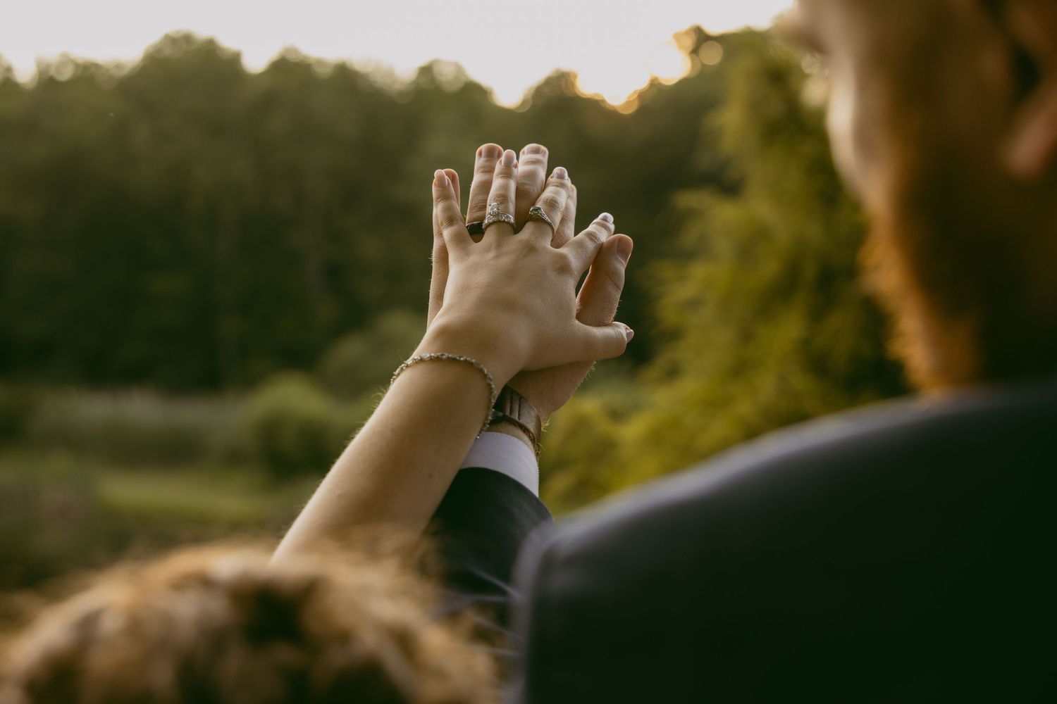 Silhouetted hands reaching toward sunset sky during outdoor wedding celebration.