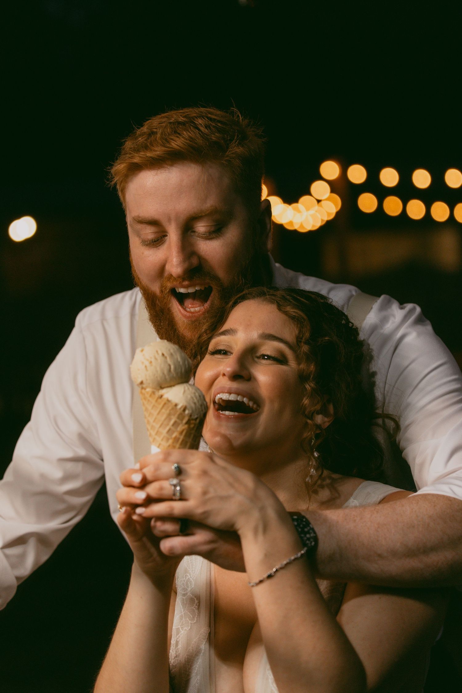 A couple shares a joyful moment while eating ice cream together with bokeh lights glowing in the background.