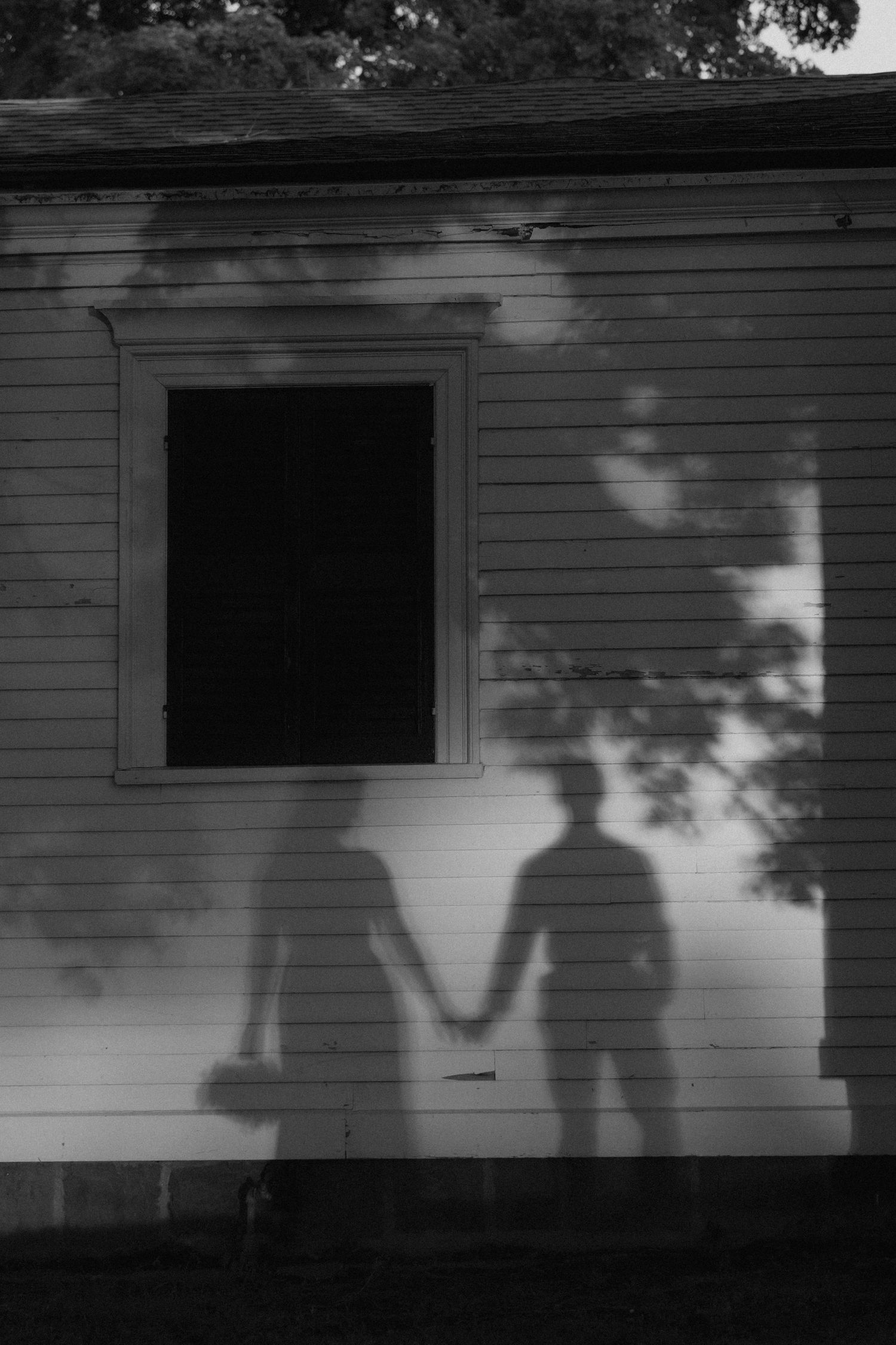 Black and white photo of two shadows holding hands cast on a house wall next to a dark doorway.