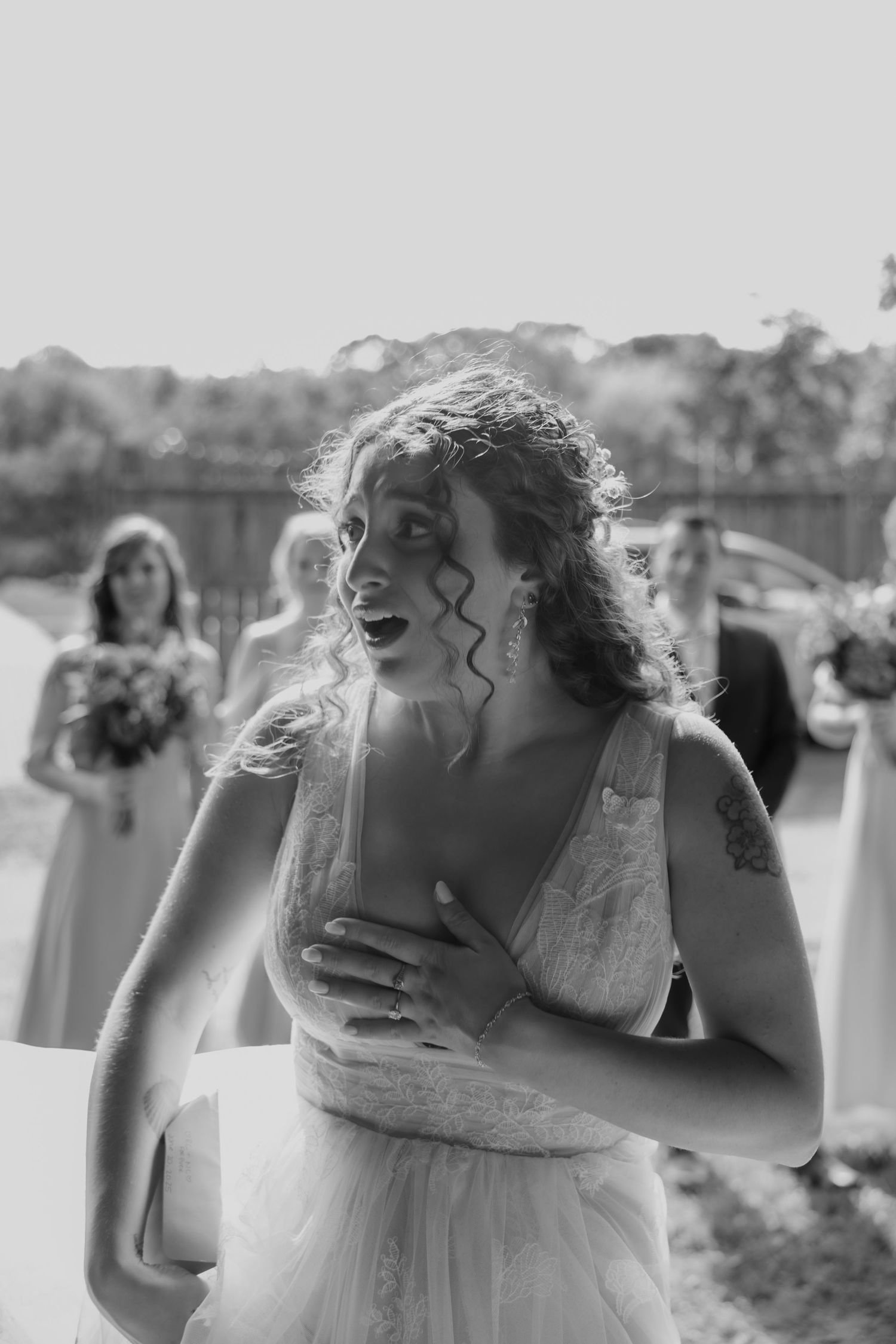 Black and white wedding photography captures an emotional moment in natural light with white dress and curly hair.