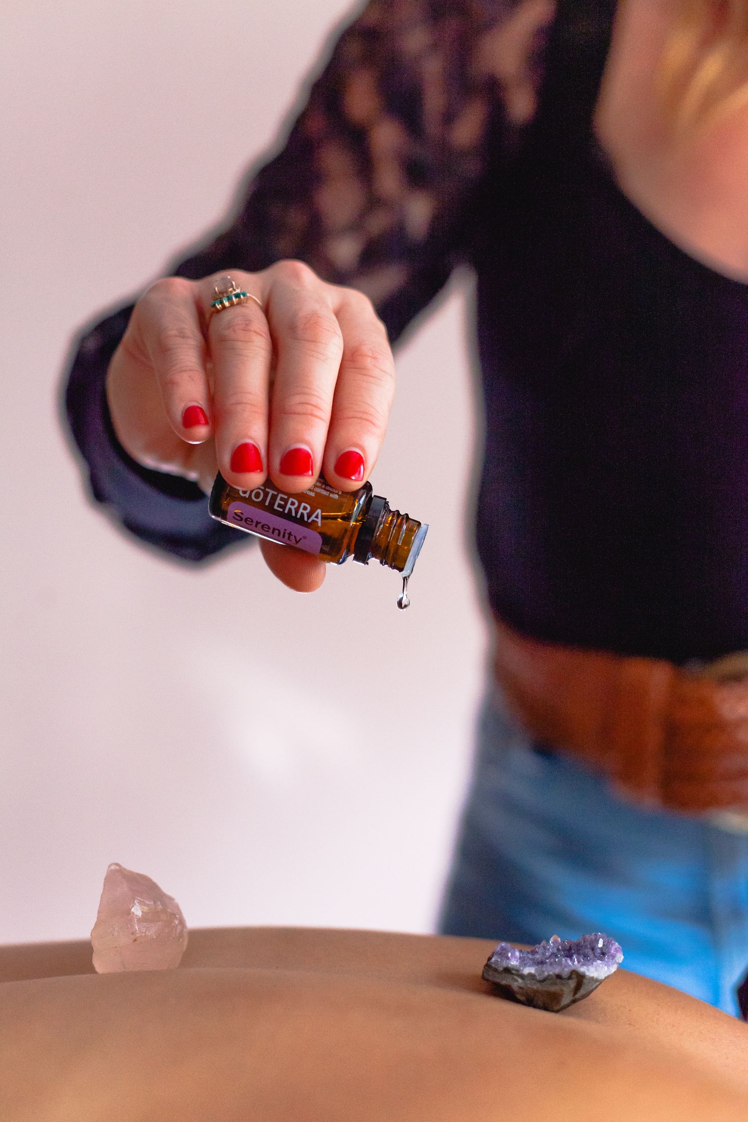 Close-up of hands with red nails dropping essential oil onto crystals during spa treatment.