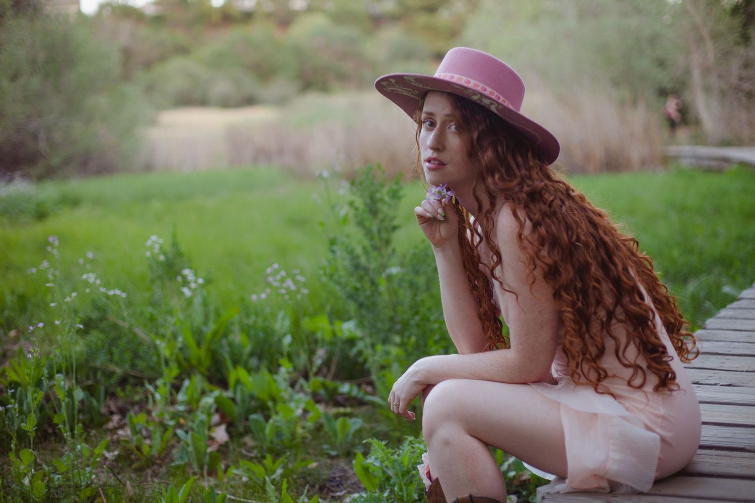 Artistic outdoor portrait with pink hat and flowing dress in garden setting.