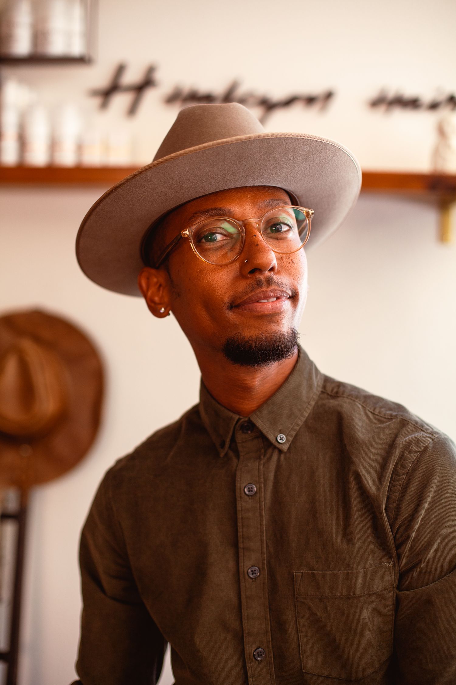 Stylish individual wearing glasses and fedora hat in brown tones against salon wall.