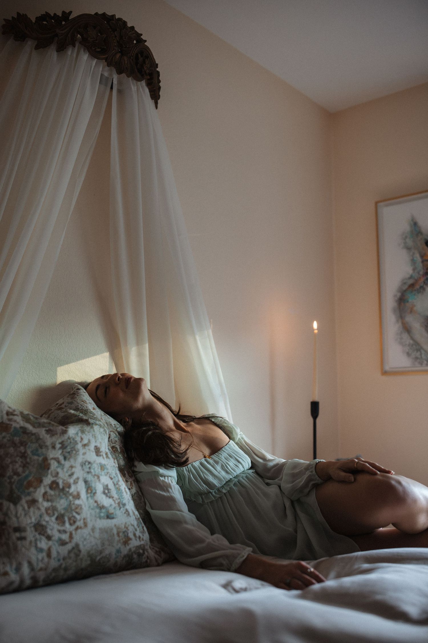 A person lies in bed under soft white curtains and natural light streaming through a window in a peaceful bedroom scene.